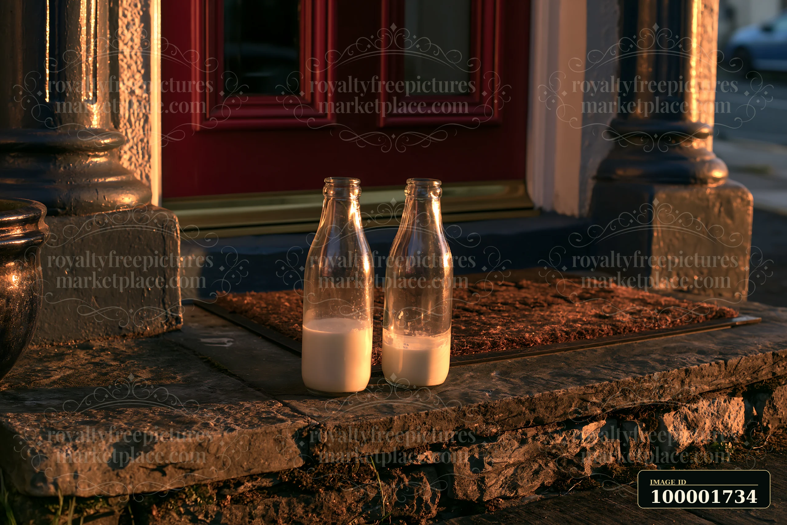 Two glass milk bottles sit on a doorstep in front of a red door as the sun rises.