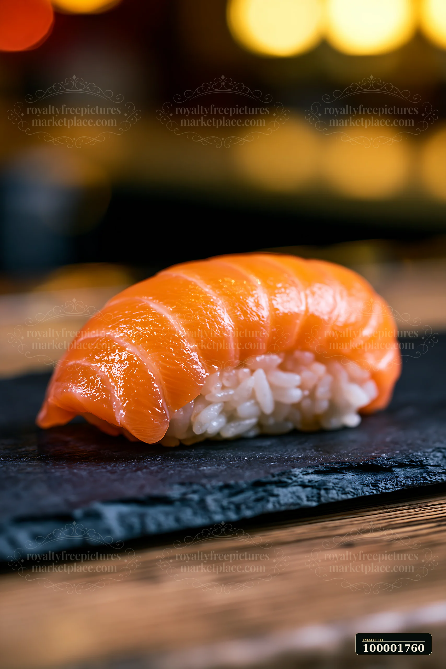 One salmon nigiri on slate plate sits on a wooden table.