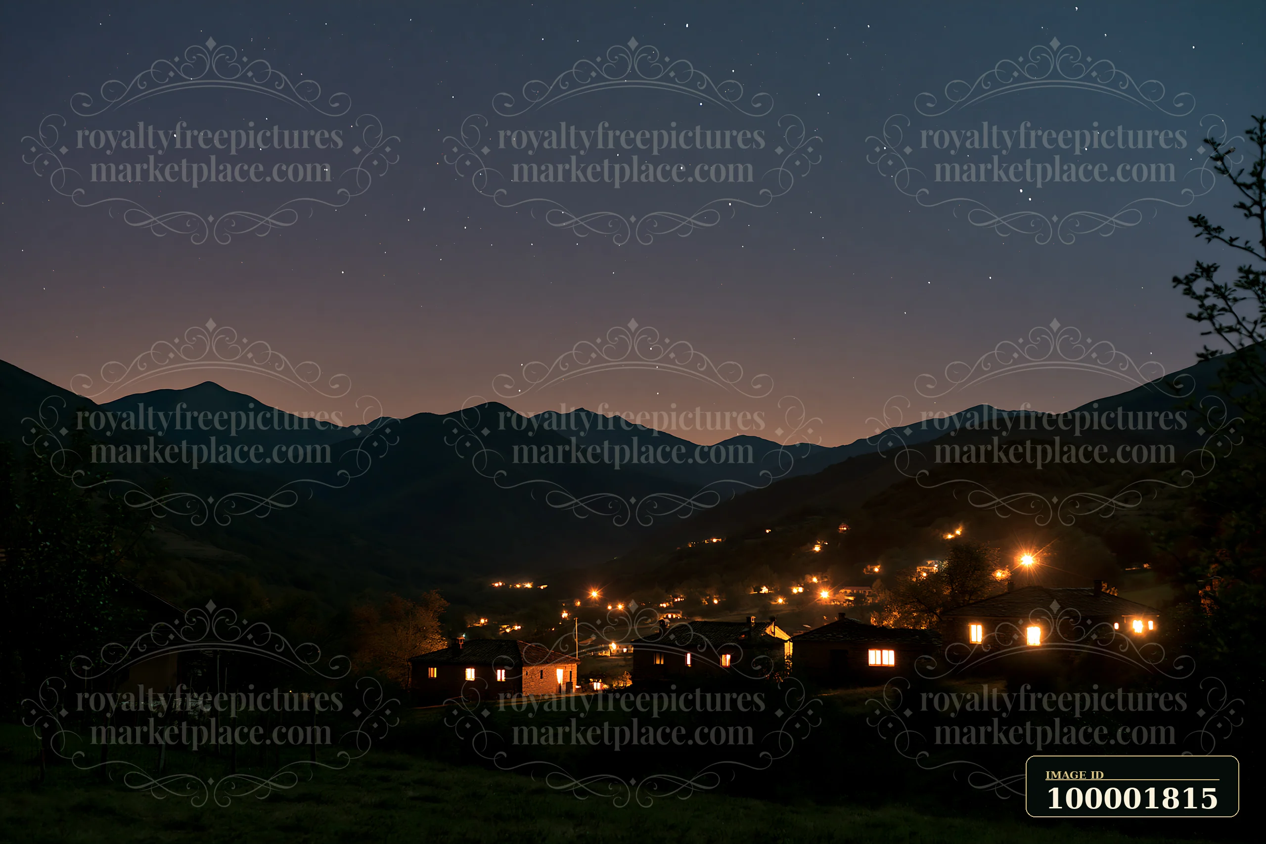 Stars fill the night sky above a mountain valley where houses glow with warm light.