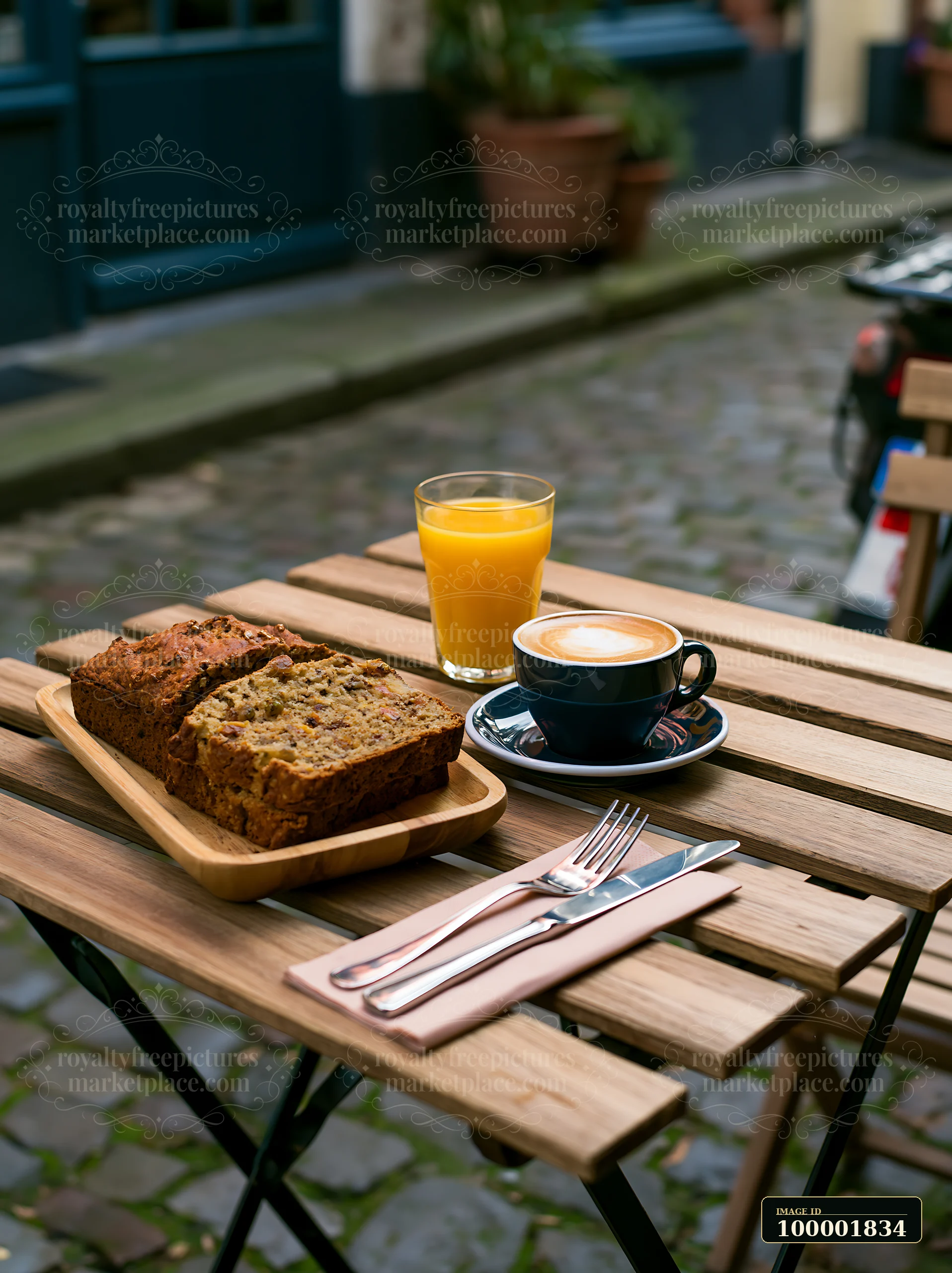 A street cafe table features milk coffee, sliced bread, and orange juice set on a cobblestone street.