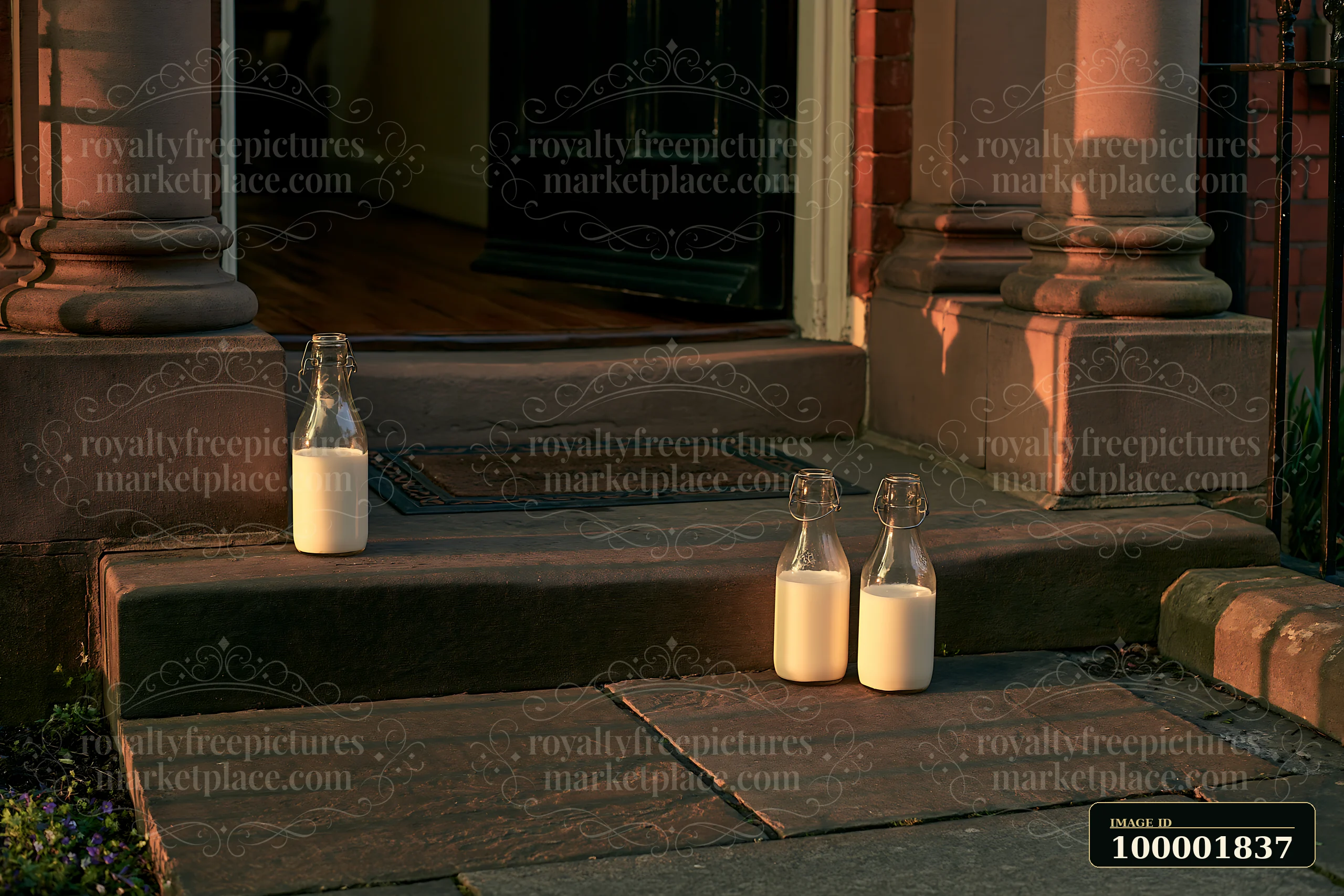 Two glass milk bottles sit on the stone steps of a home as the sun rises, casting warm light on the doorstep and highlighting the bottles' contents.