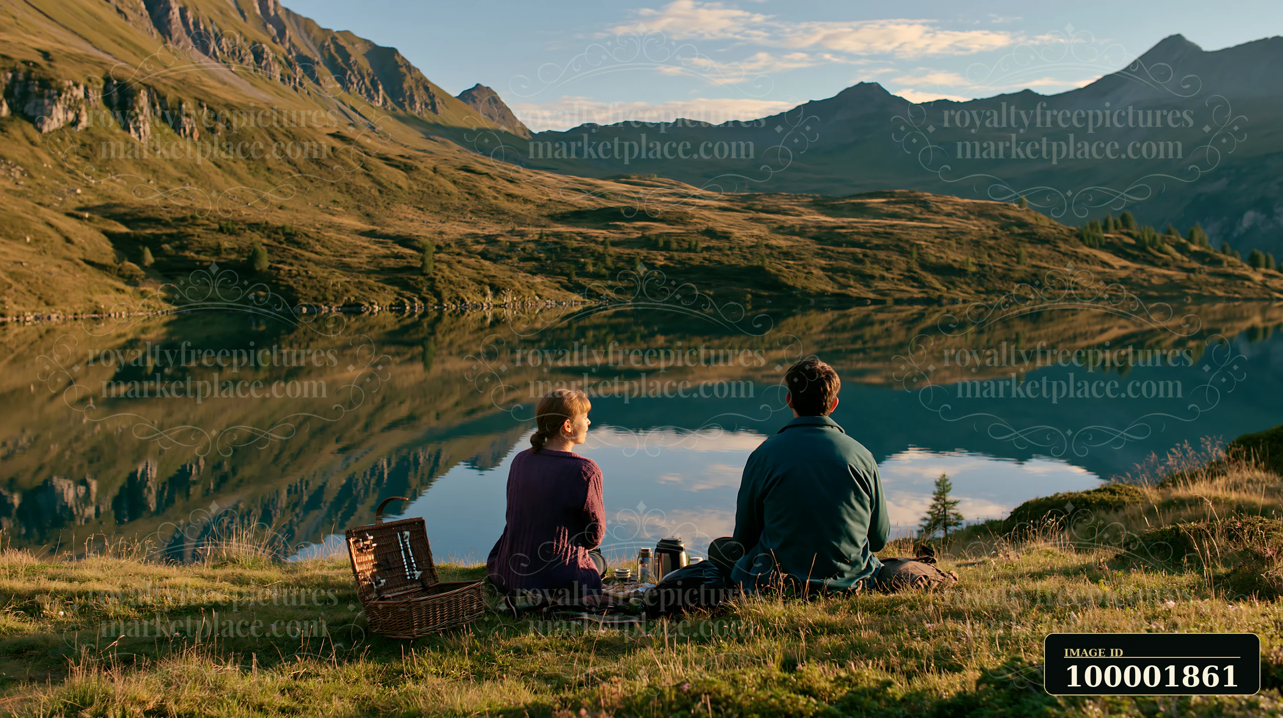 Two people sit on the grass near an alpine lake in Switzerland, sharing a picnic while enjoying the view of mountains and reflections on the water.