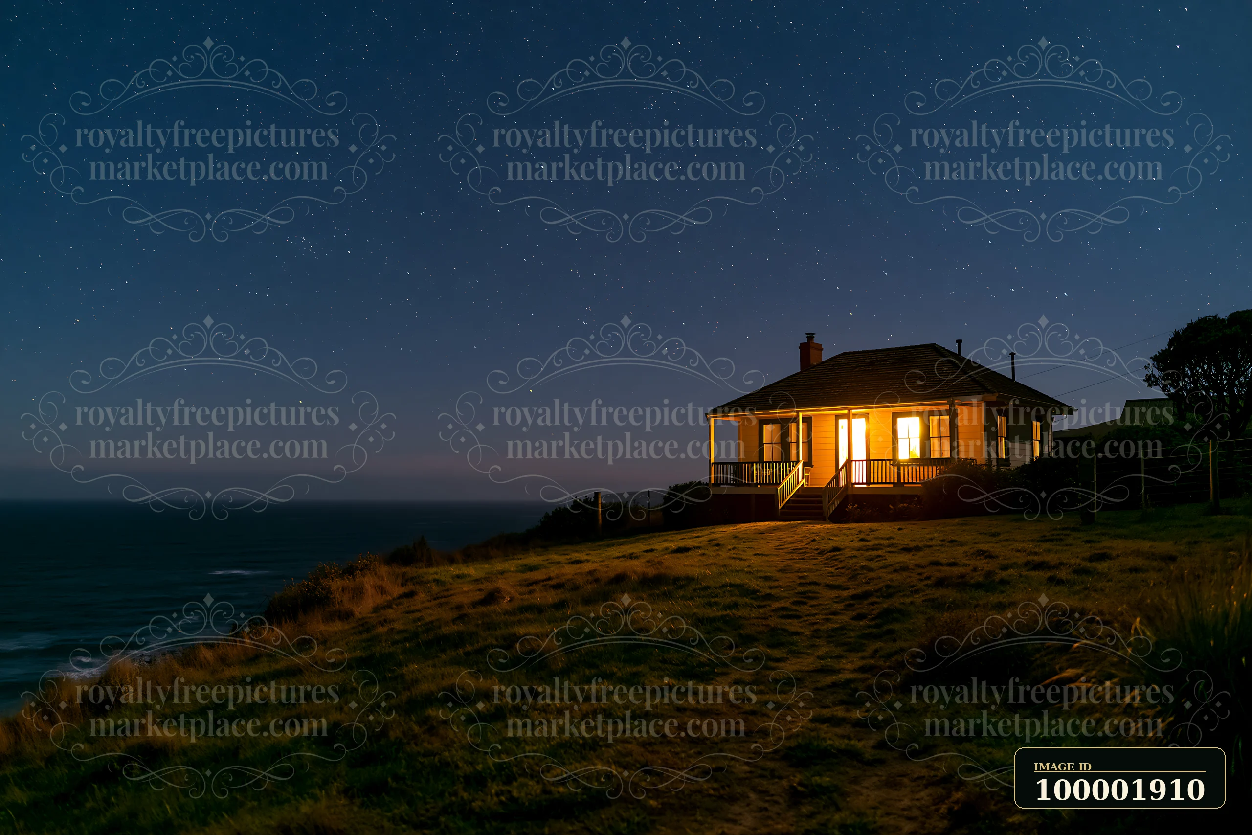 A villa stands illuminated on a hillside, surrounded by grass and facing the ocean.