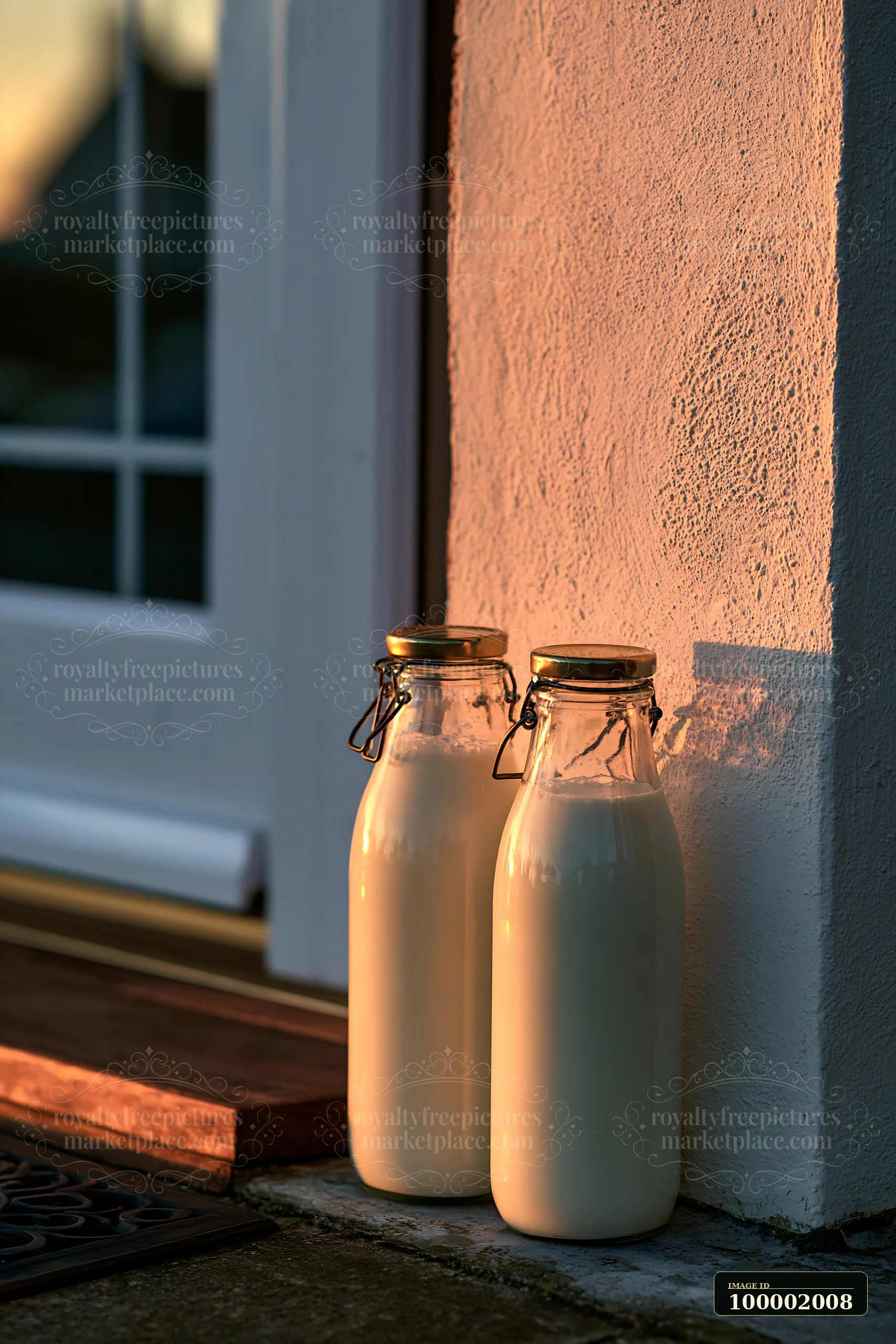 Two glass milk bottles sit on a doorstep, illuminated by the warm light of the rising sun.