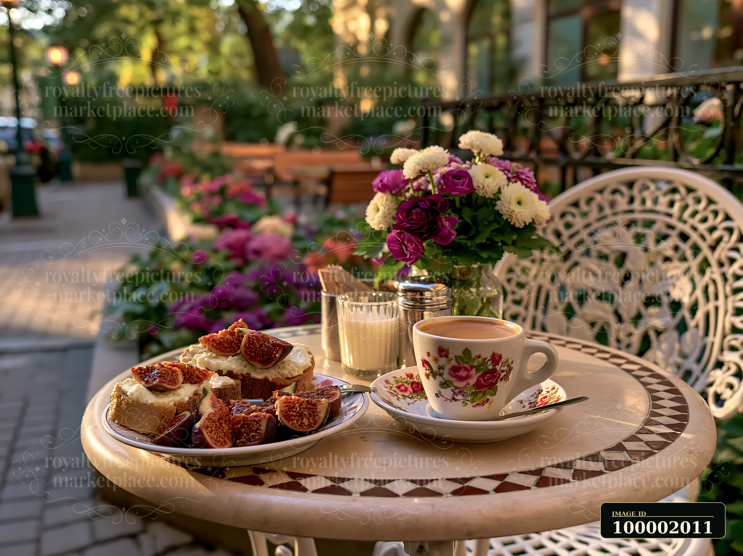 A small round table at a street cafe features a cup of milk coffee alongside a plate of bread topped with figs and a glass of juice.