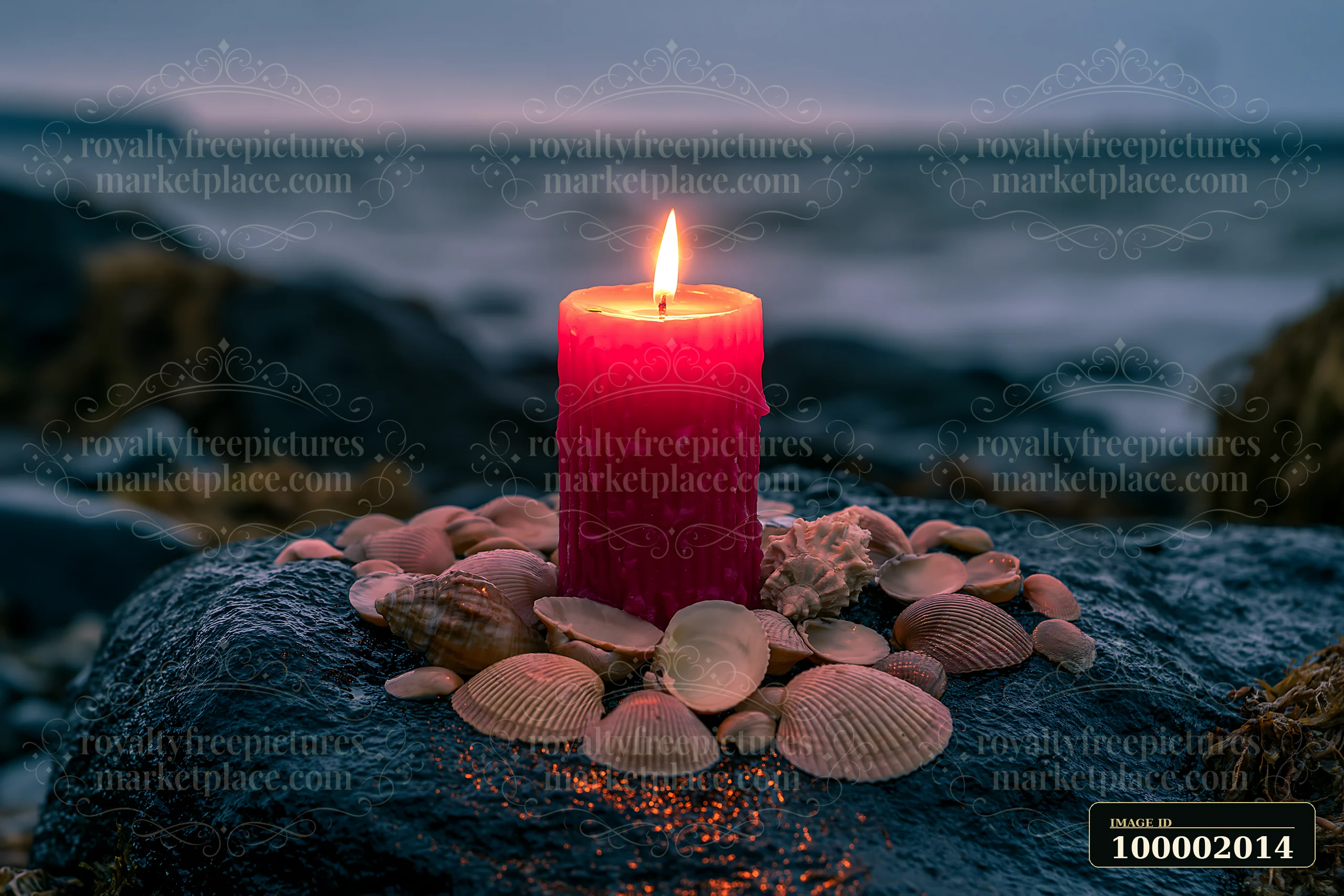A red candle burns in the center of seashells arranged on a rock by the ocean.