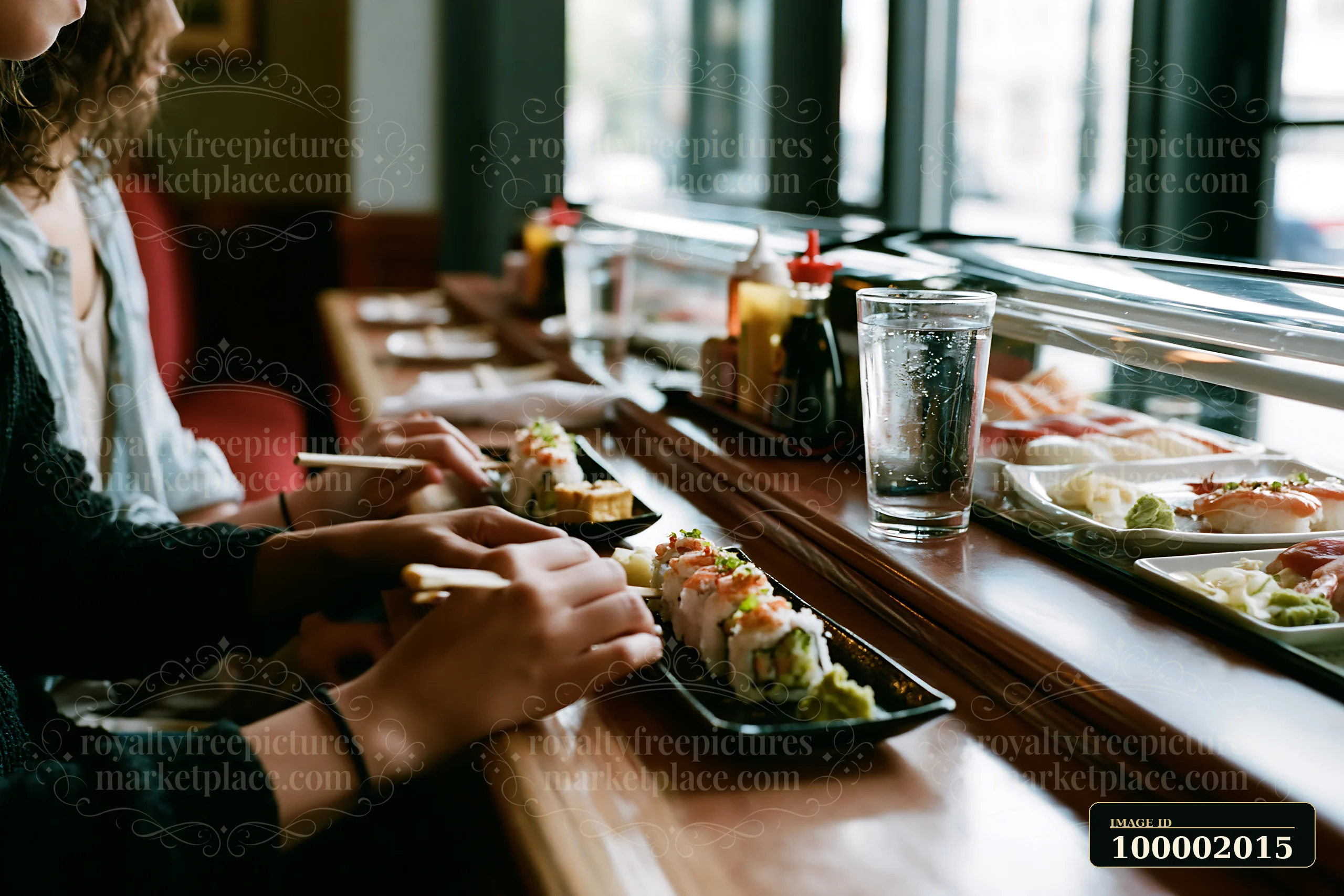 Two people enjoy a romantic sushi dinner at a wooden table by a window.