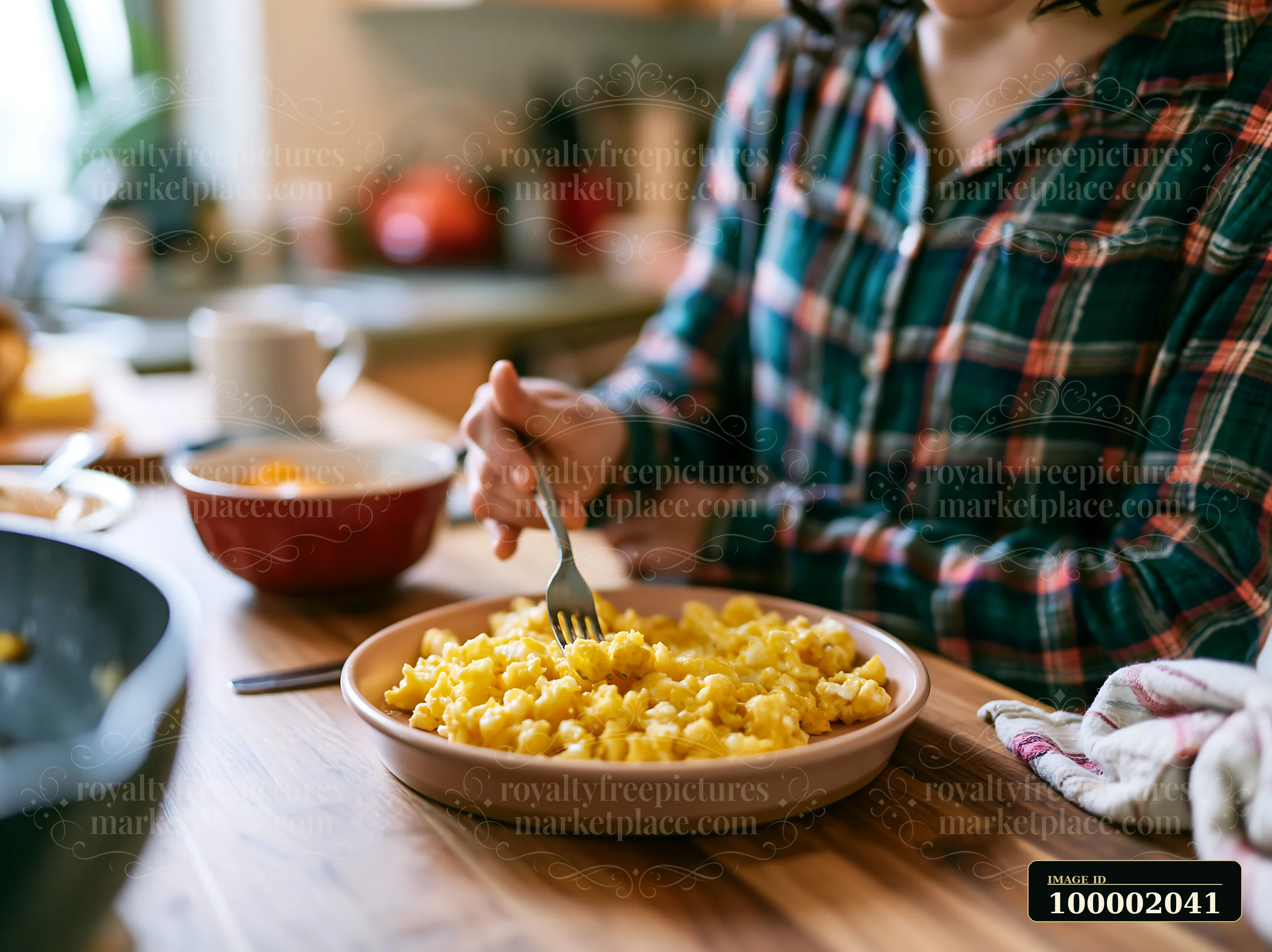 A person with limited hand mobility using utensils eats pasta in a kitchen setting with various dishware on a wooden table.