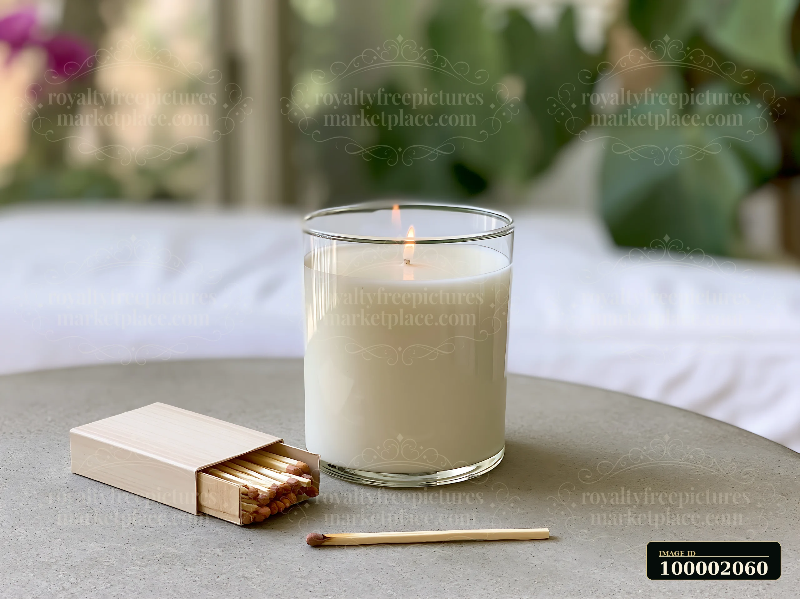 A glass candle with two wicks sits on a neutral table with a box of matches beside it.