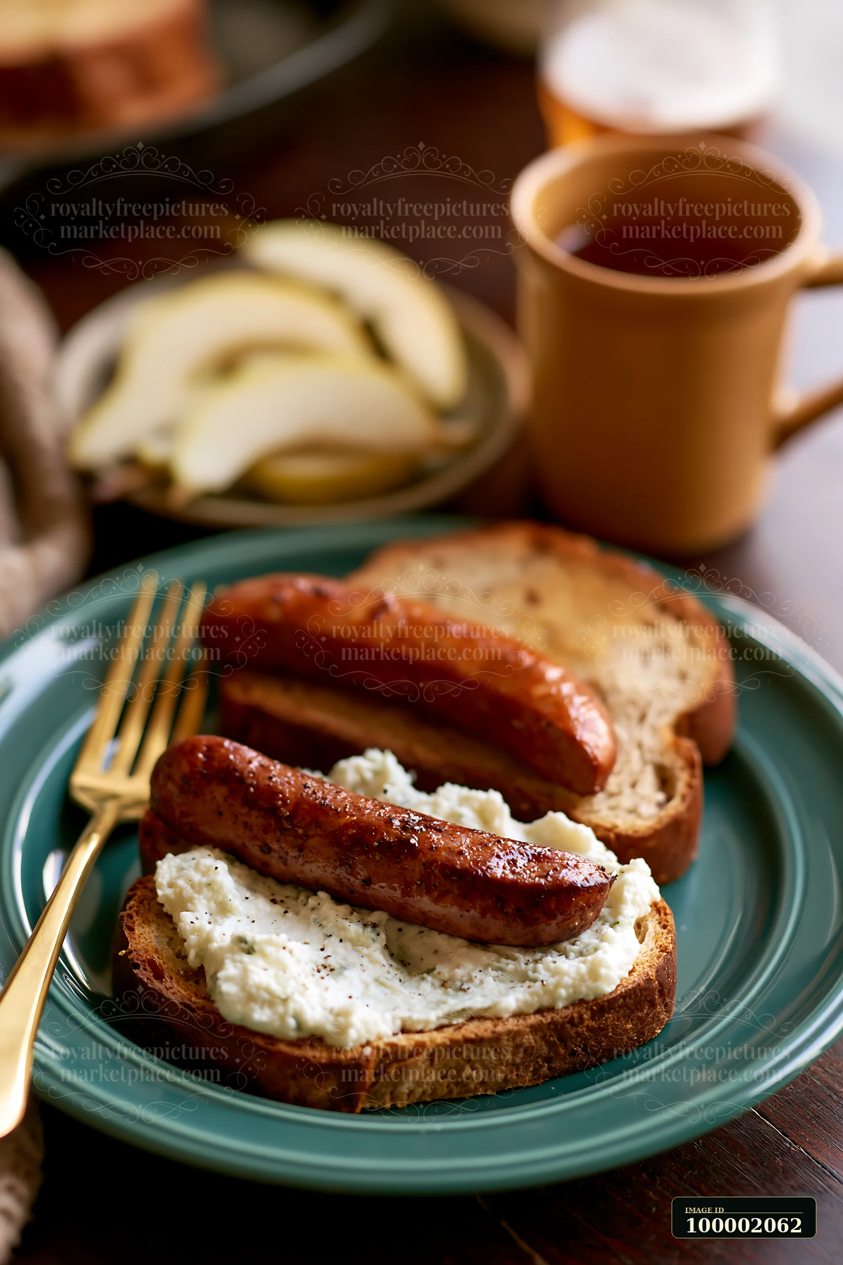 A breakfast plate with sausage sits on a green dish alongside a cup of tea.