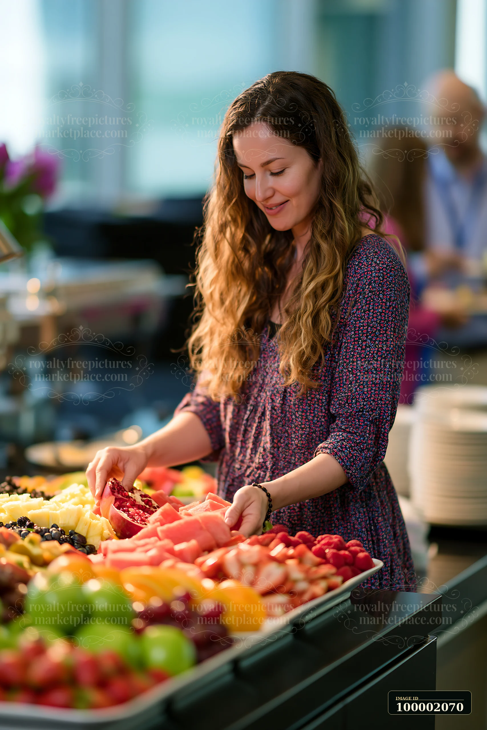 A woman selects fresh fruit from a large buffet table during a corporate lunch buffet.