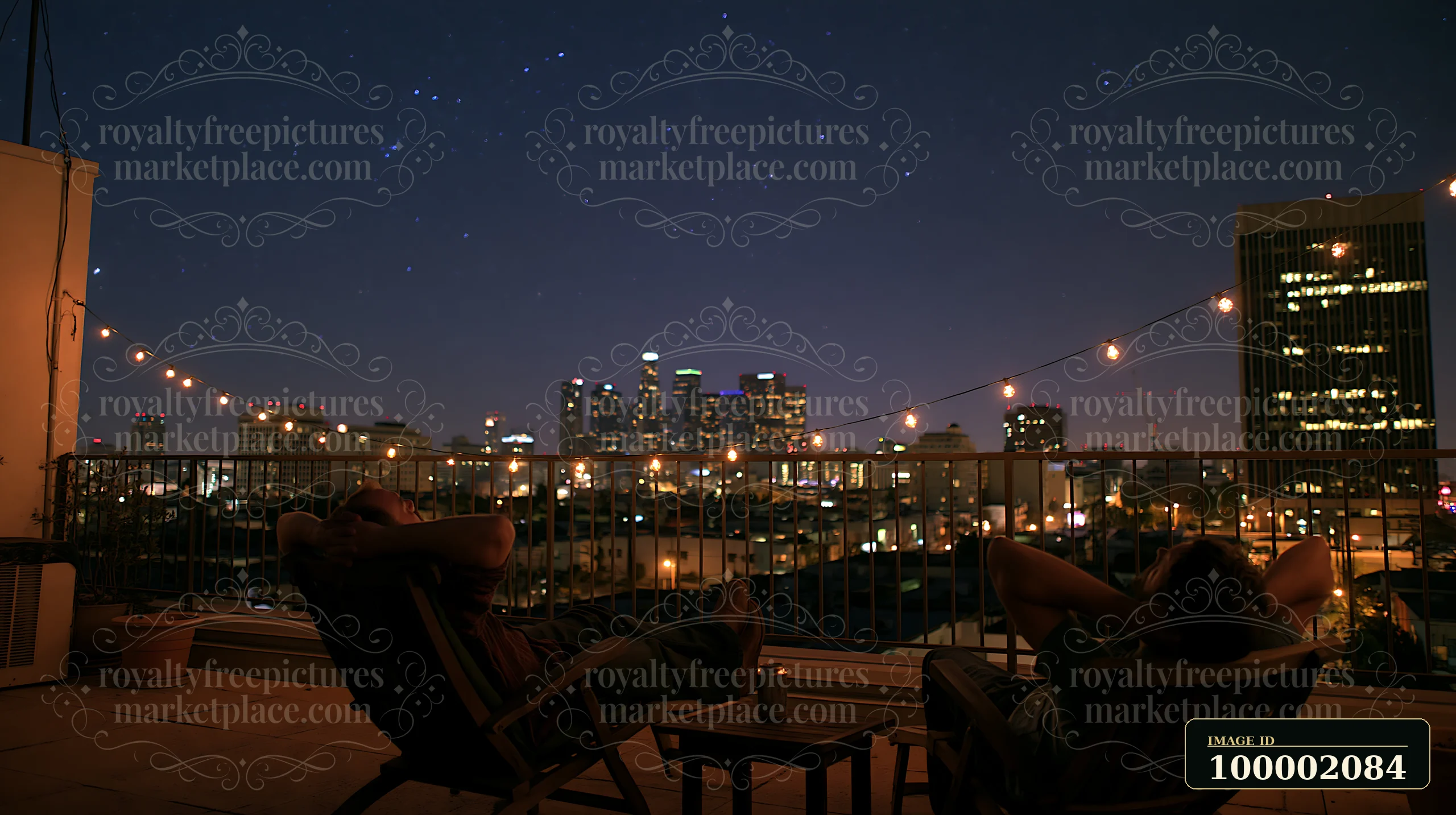 Under a starry night over a person watching the sky, two people relax on a rooftop with a view of the city skyline.