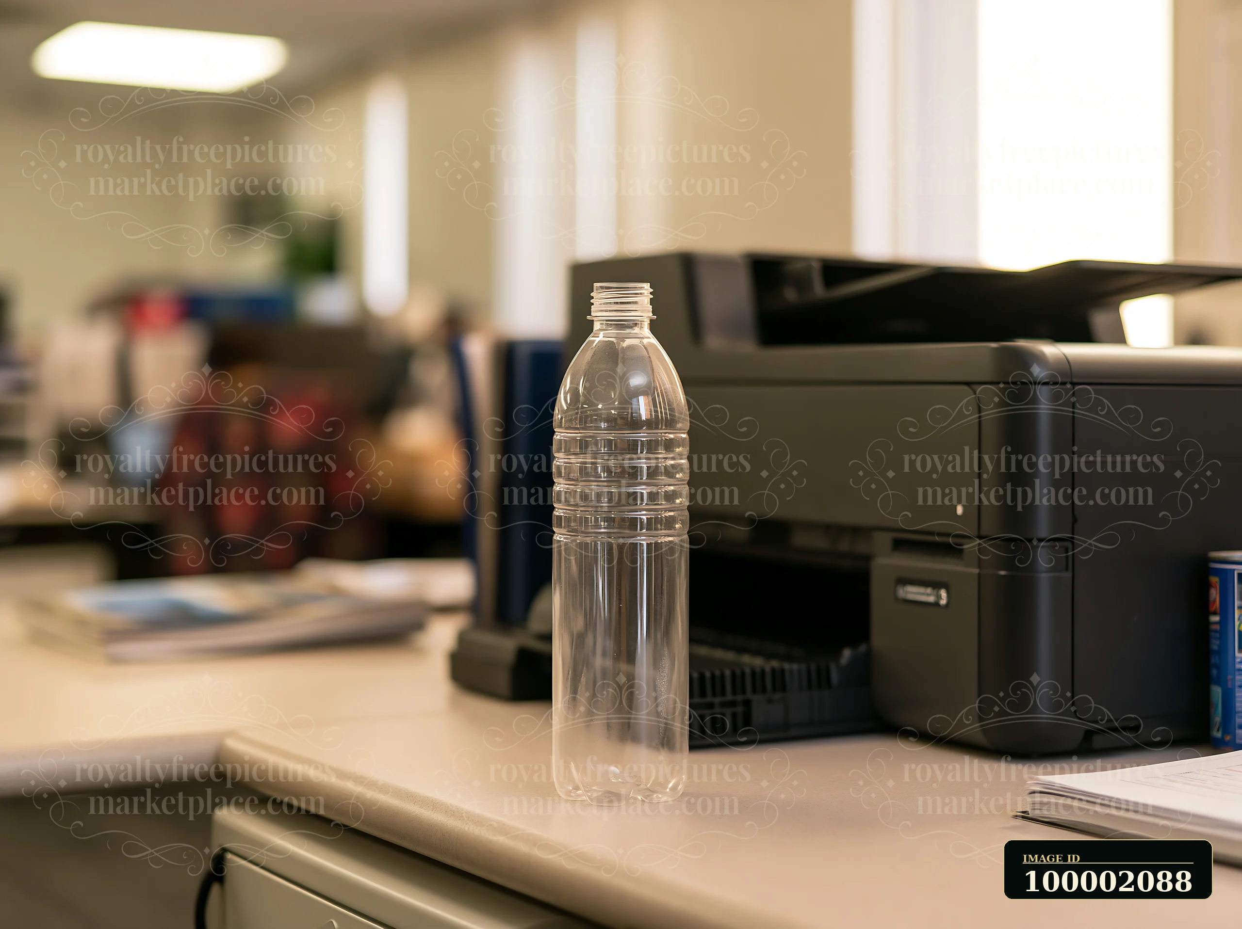 An empty bottle stands on a desk in an office space with a printer nearby.