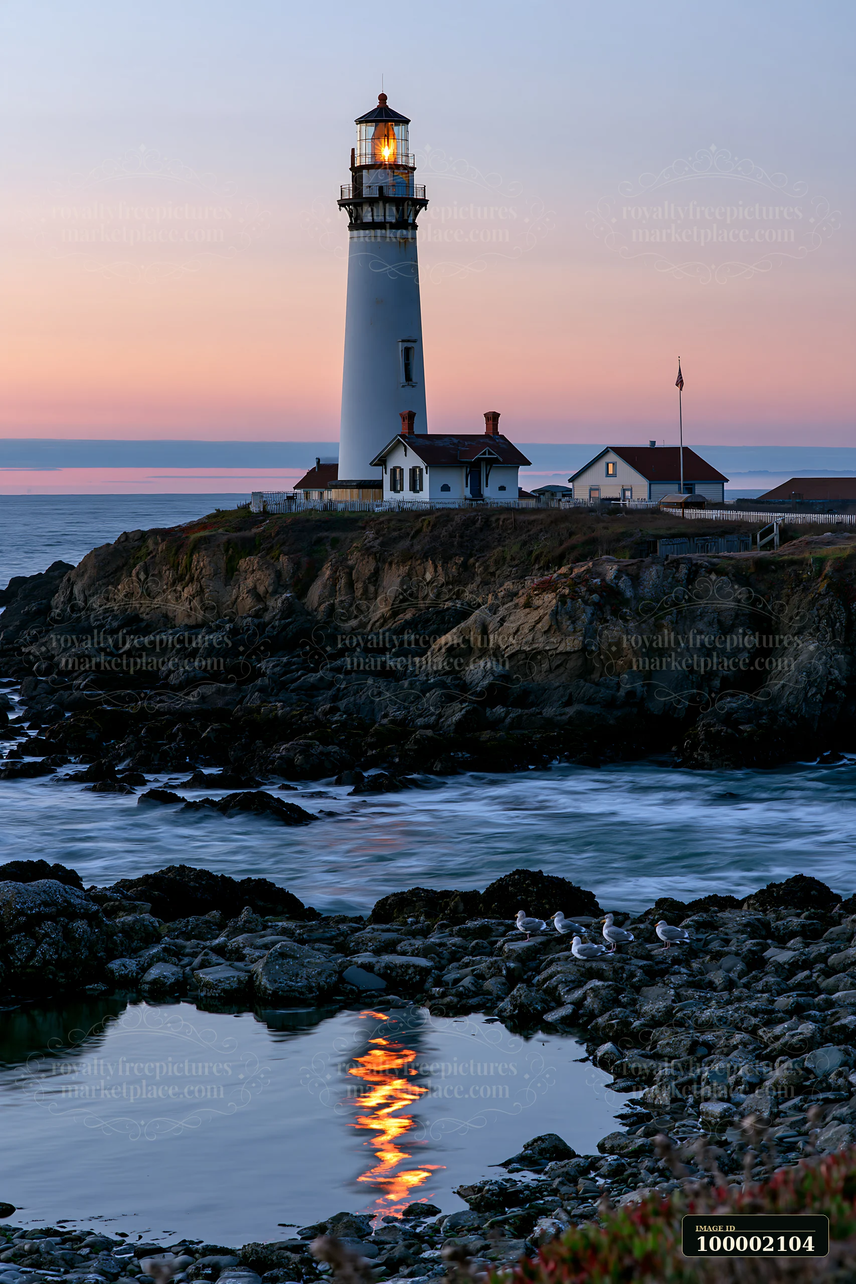 The lighthouse near a rocky tide pool stands tall against the evening sky.