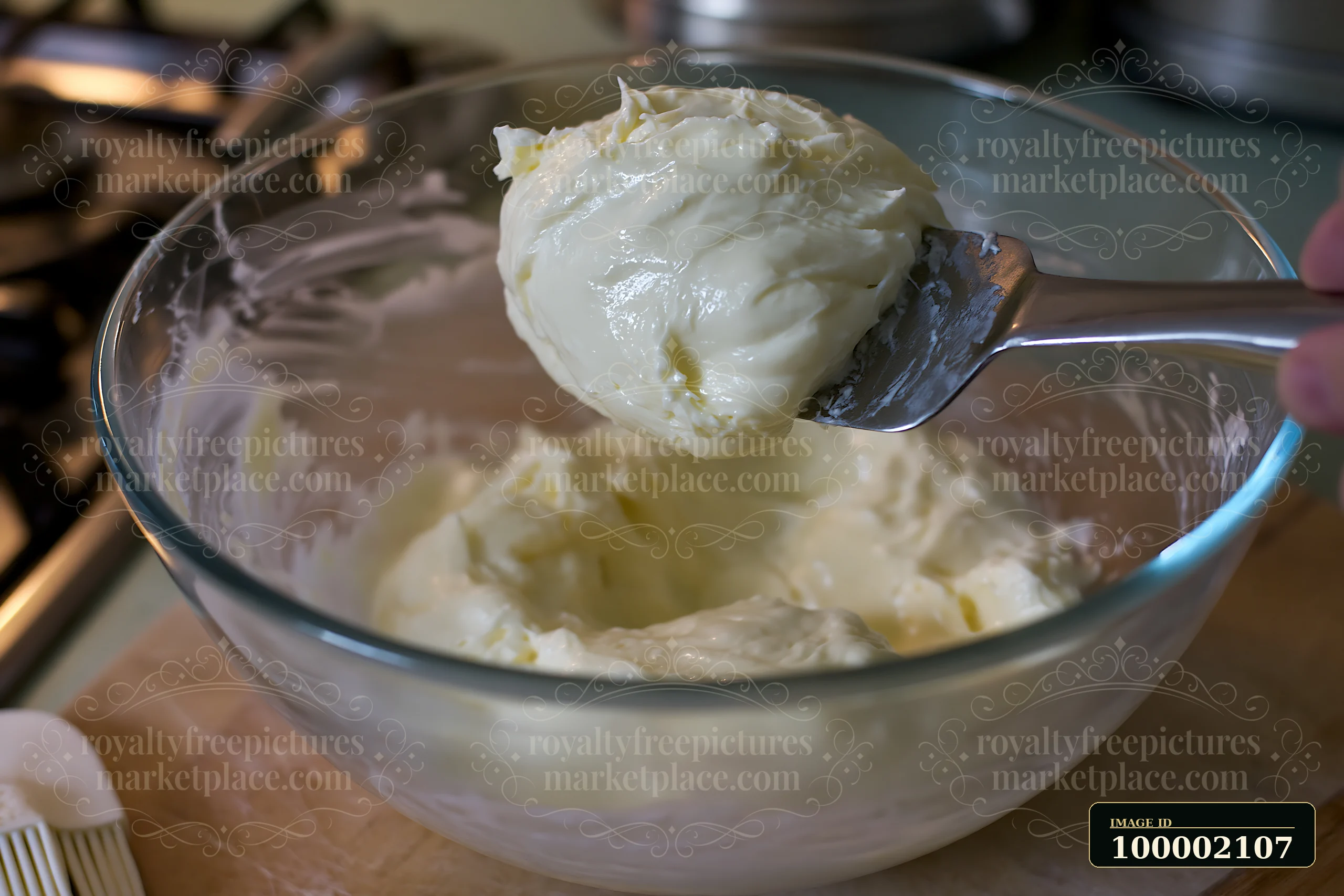 A spoon scoops cream dose with smooth glossy texture from a glass bowl in a kitchen setting.