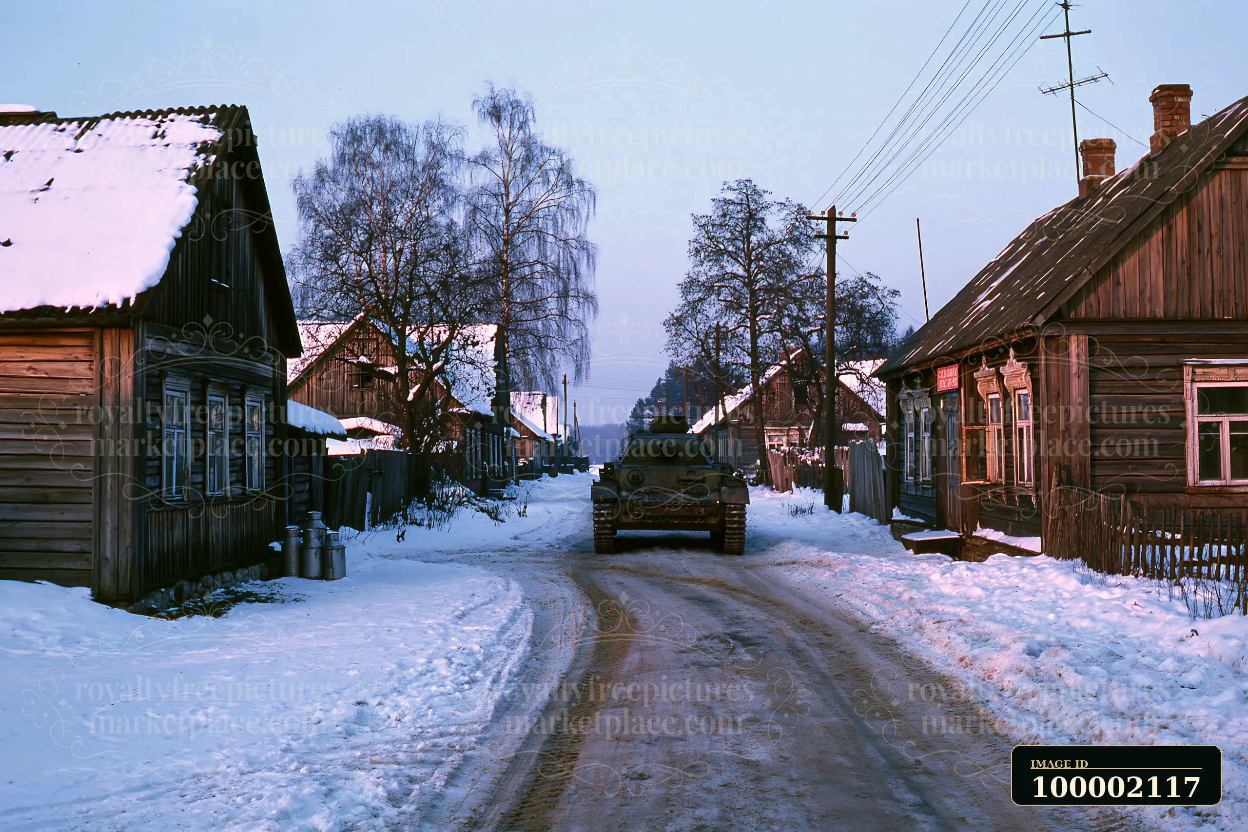 A panzer tank in winter snow travels down a dirt road lined with wooden houses.