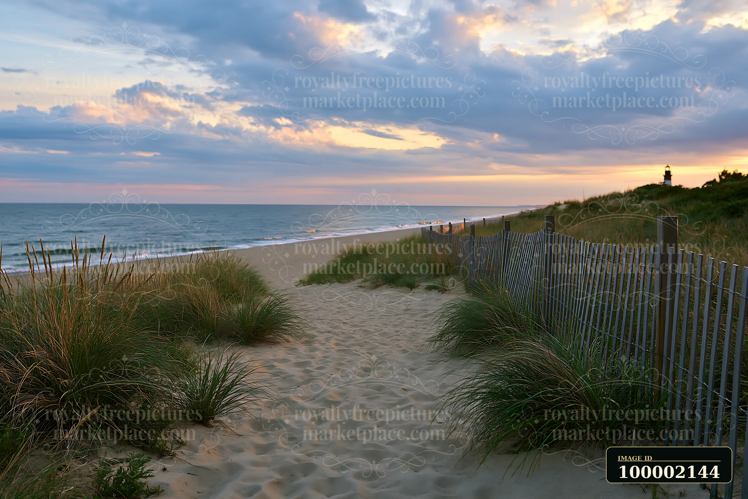 A lighthouse framed by coastal dunes stands near the shore as the sun sets, casting light on the water and clouds.