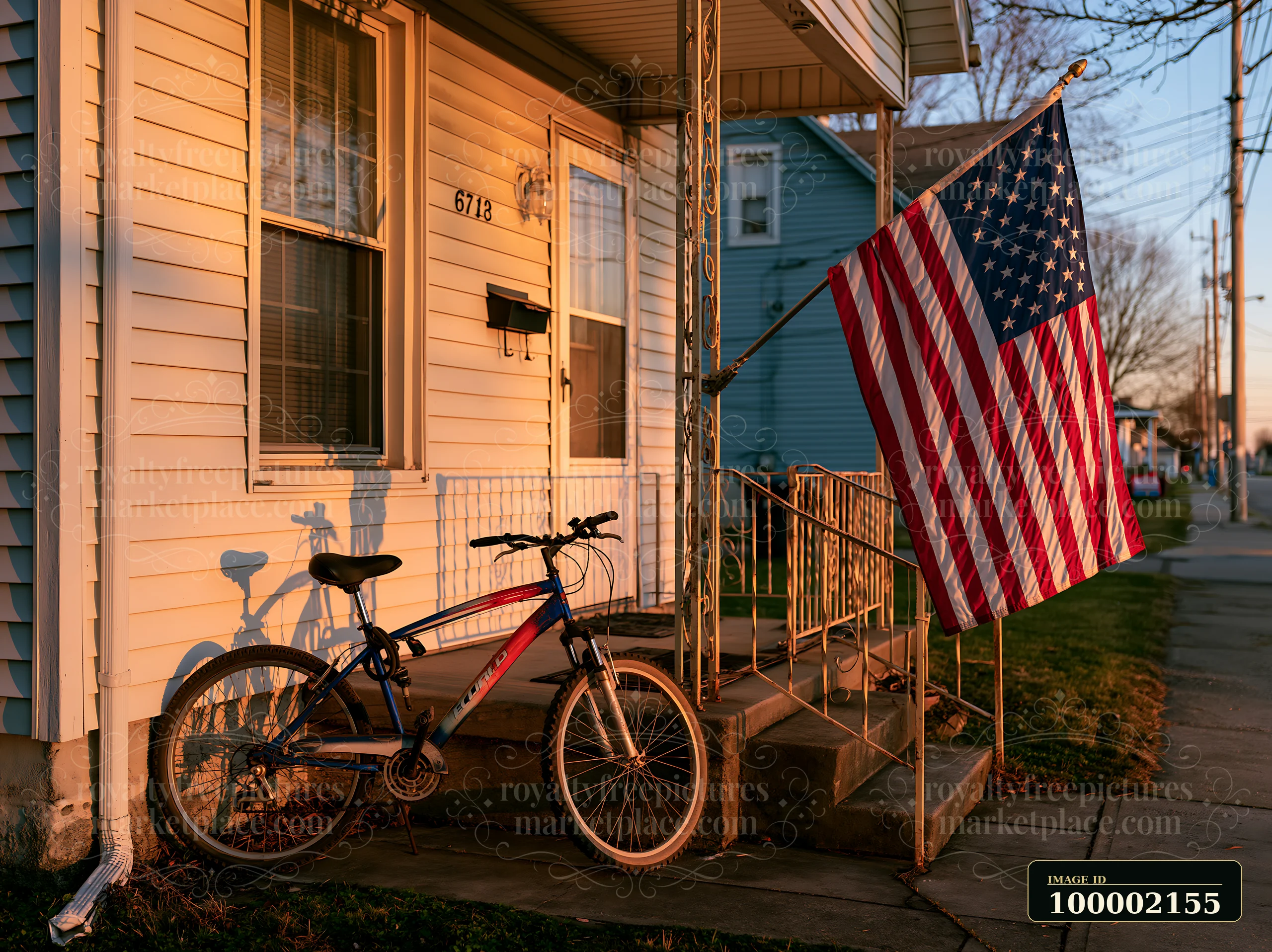 An American flag hanging from a porch stands out next to a parked bicycle during sunset.