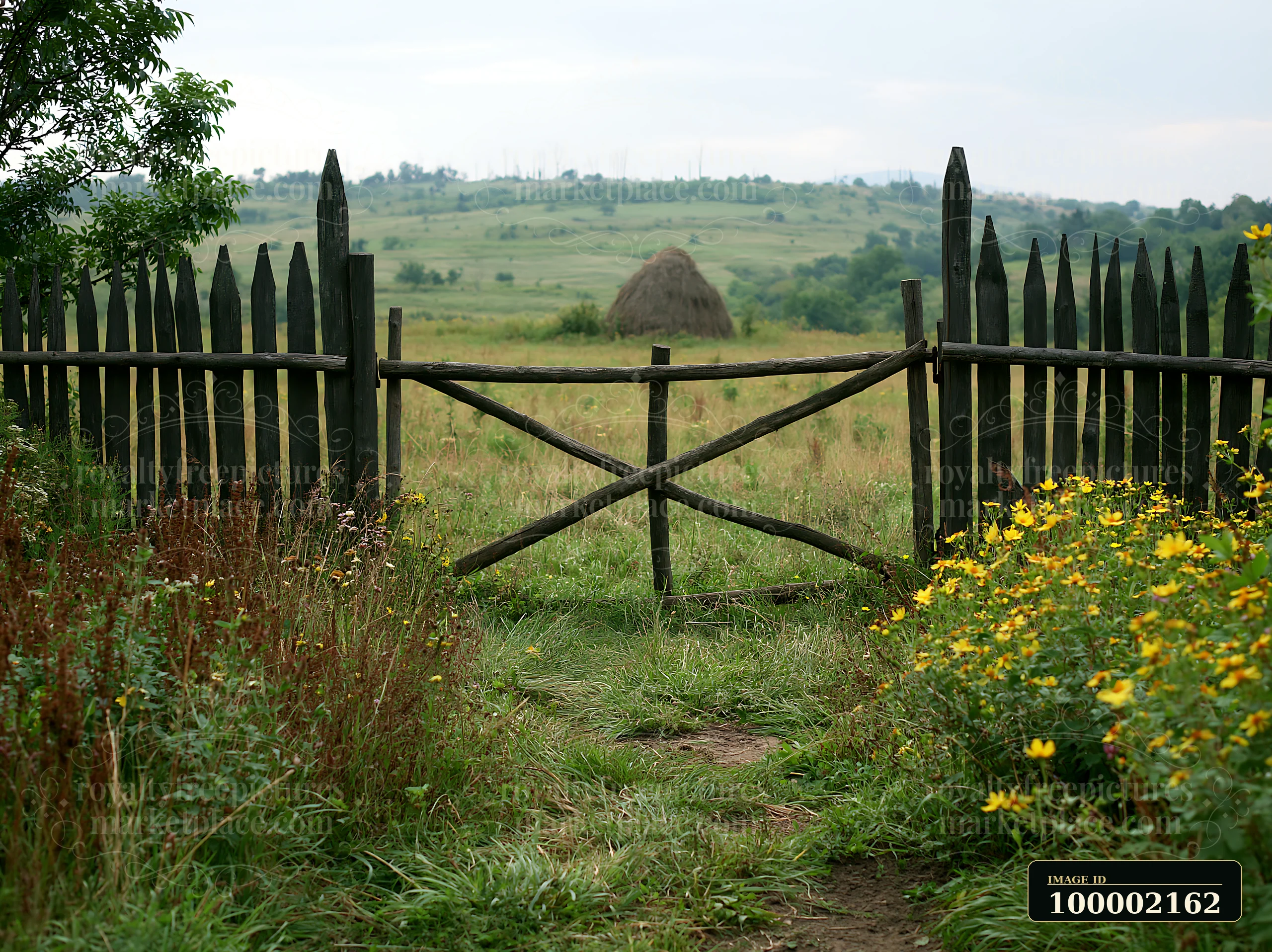 A wooden fence opens to a meadow with traditional haystack in the distance.