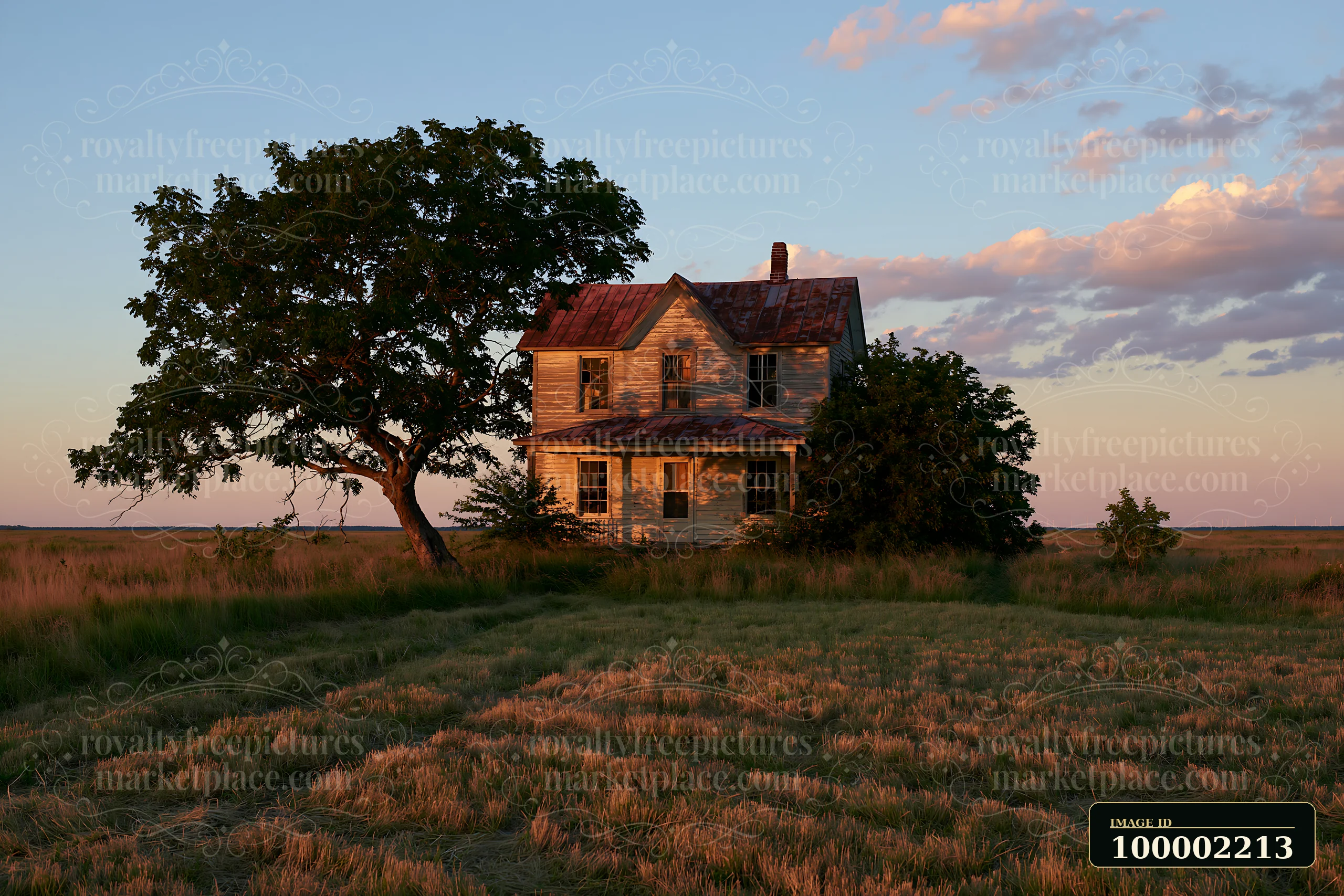 A rustic farmhouse stands under a large tree as the sun sets in a wide-open field.