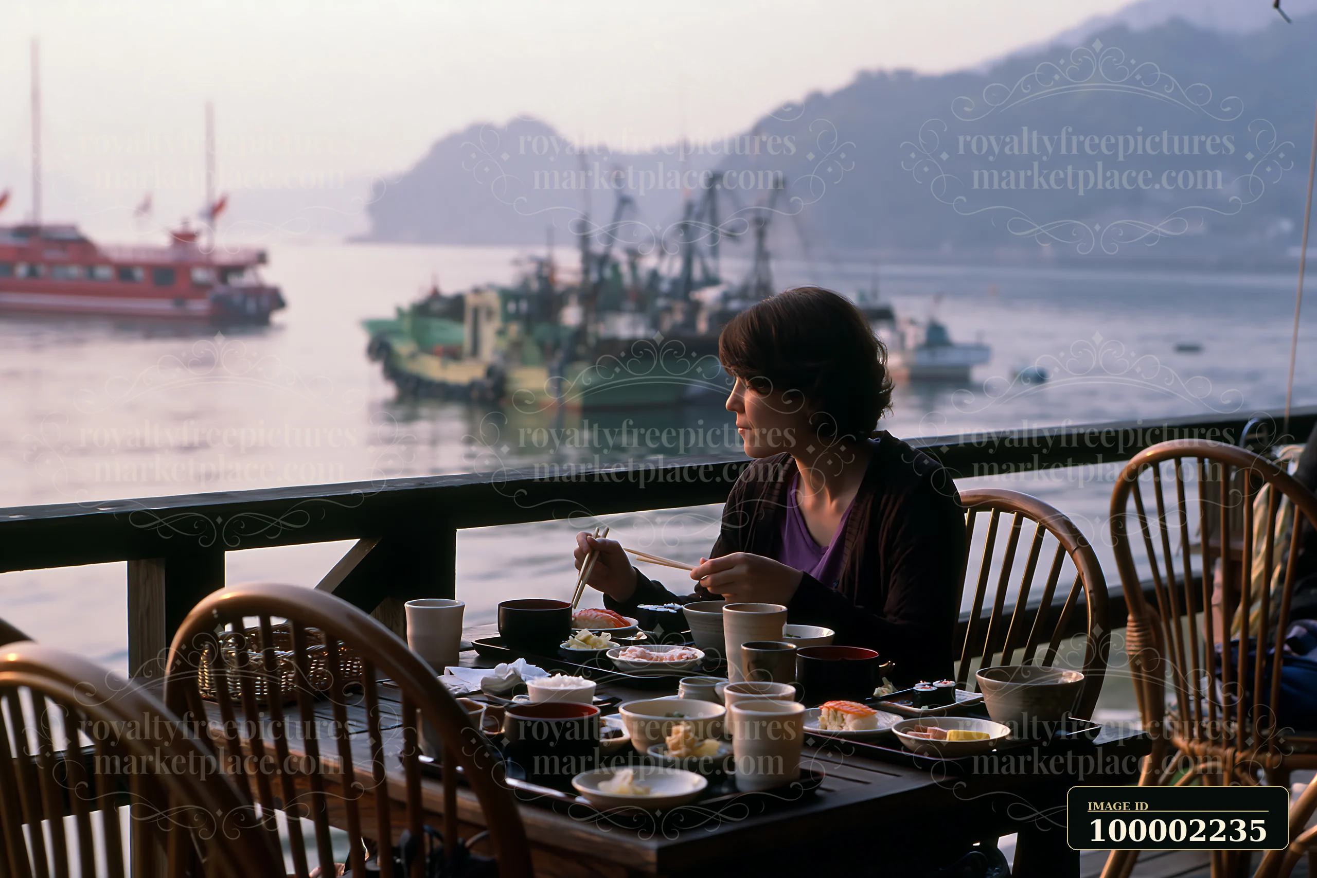 A woman eats traditional sushi breakfast in Japan while seated outside near a scenic water view.