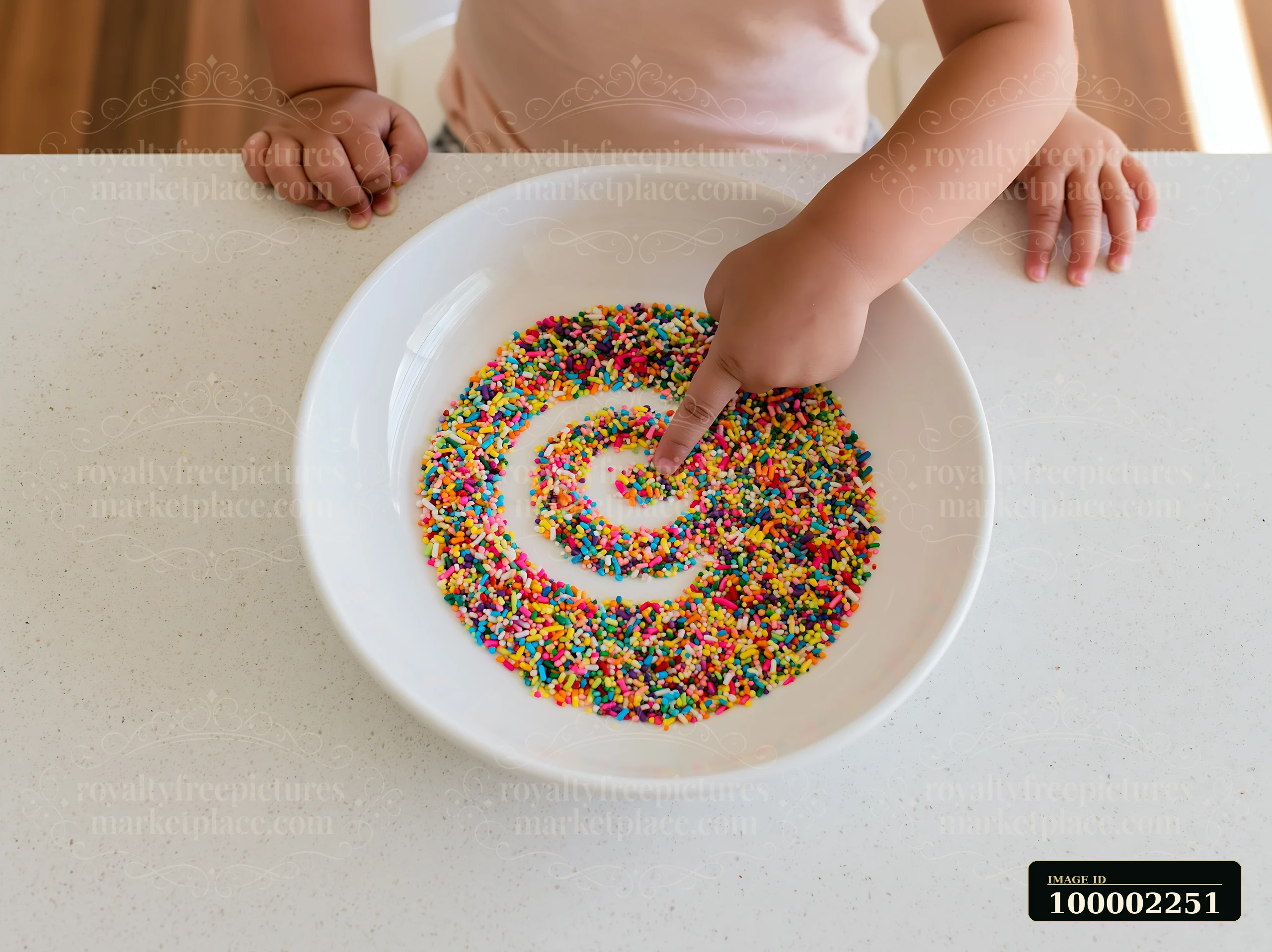 A child points to a pattern made with rainbow sprinkles arranged in a swirl on a plain white plate.