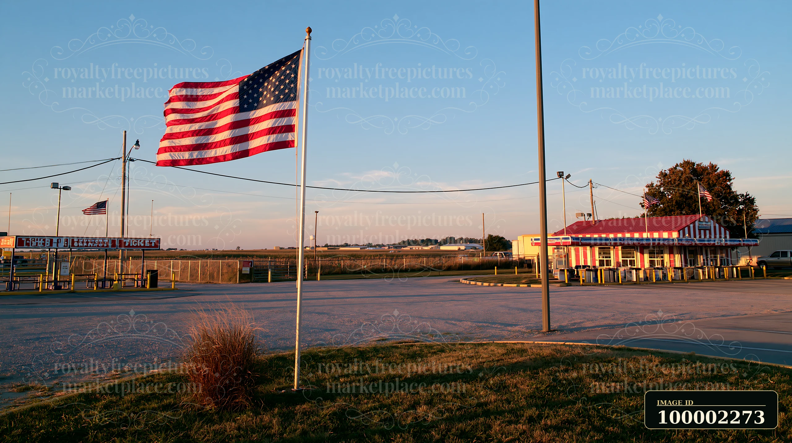 An American flag flying in strong wind stands prominently near a roadside stand.