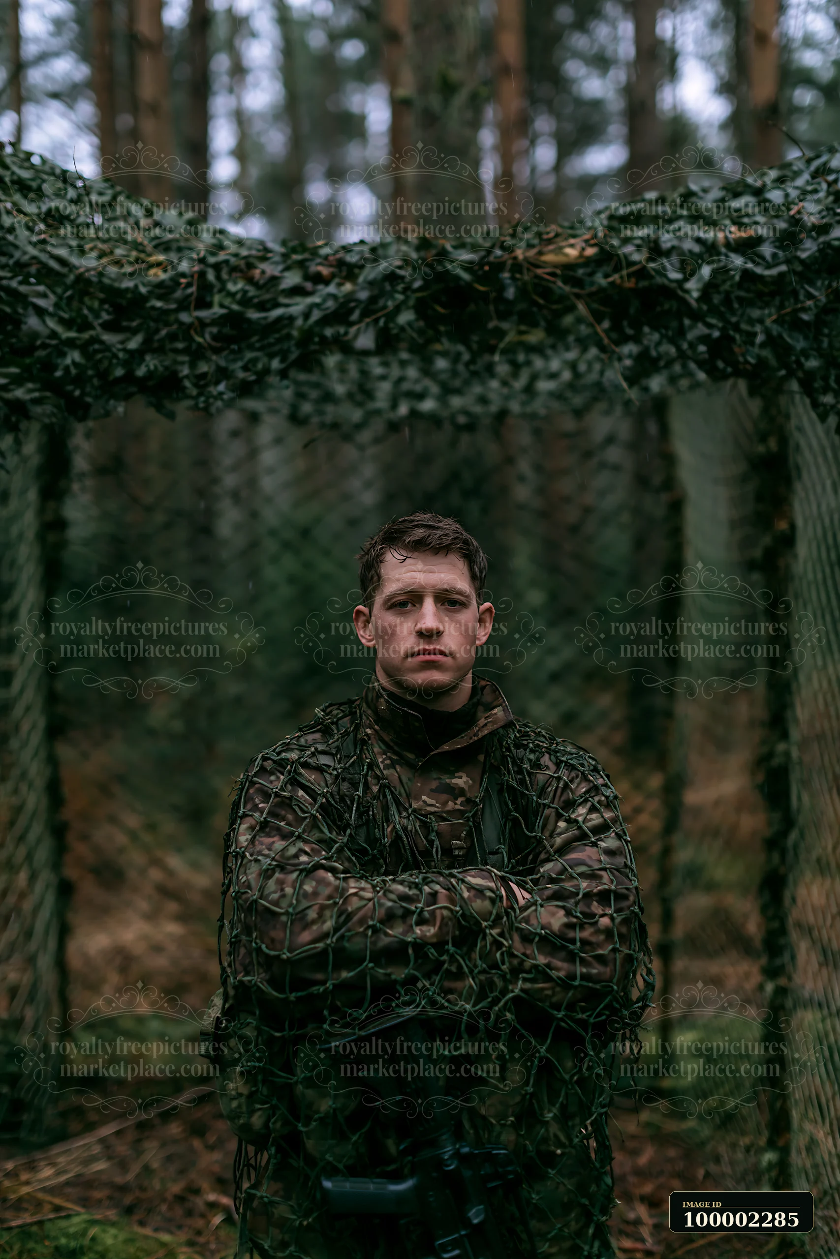 A soldier stands confidently under camouflage netting in a forest.
