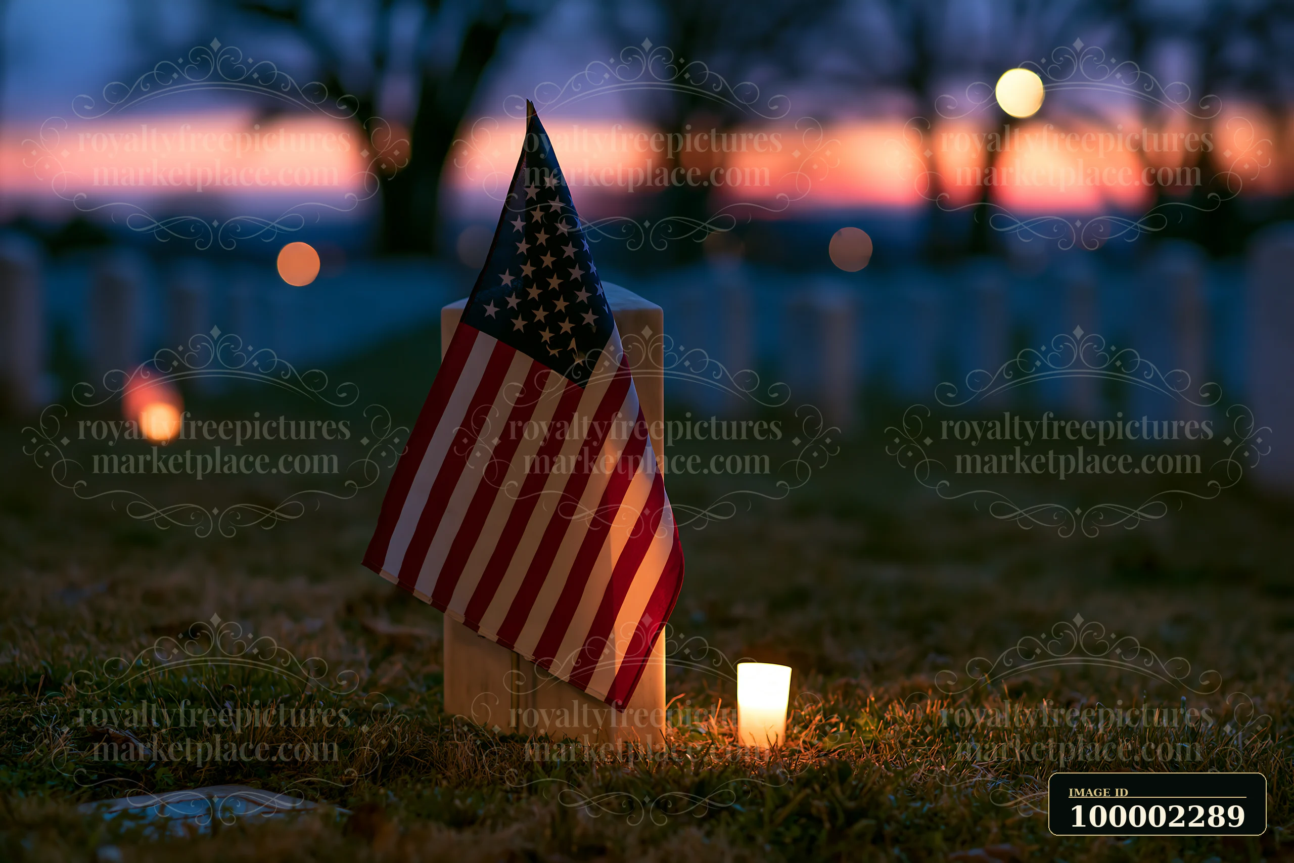 Candles light up a veterans cemetery, featuring a small American flag beside a gravestone as the sun sets, creating a solemn atmosphere under a clear night sky.