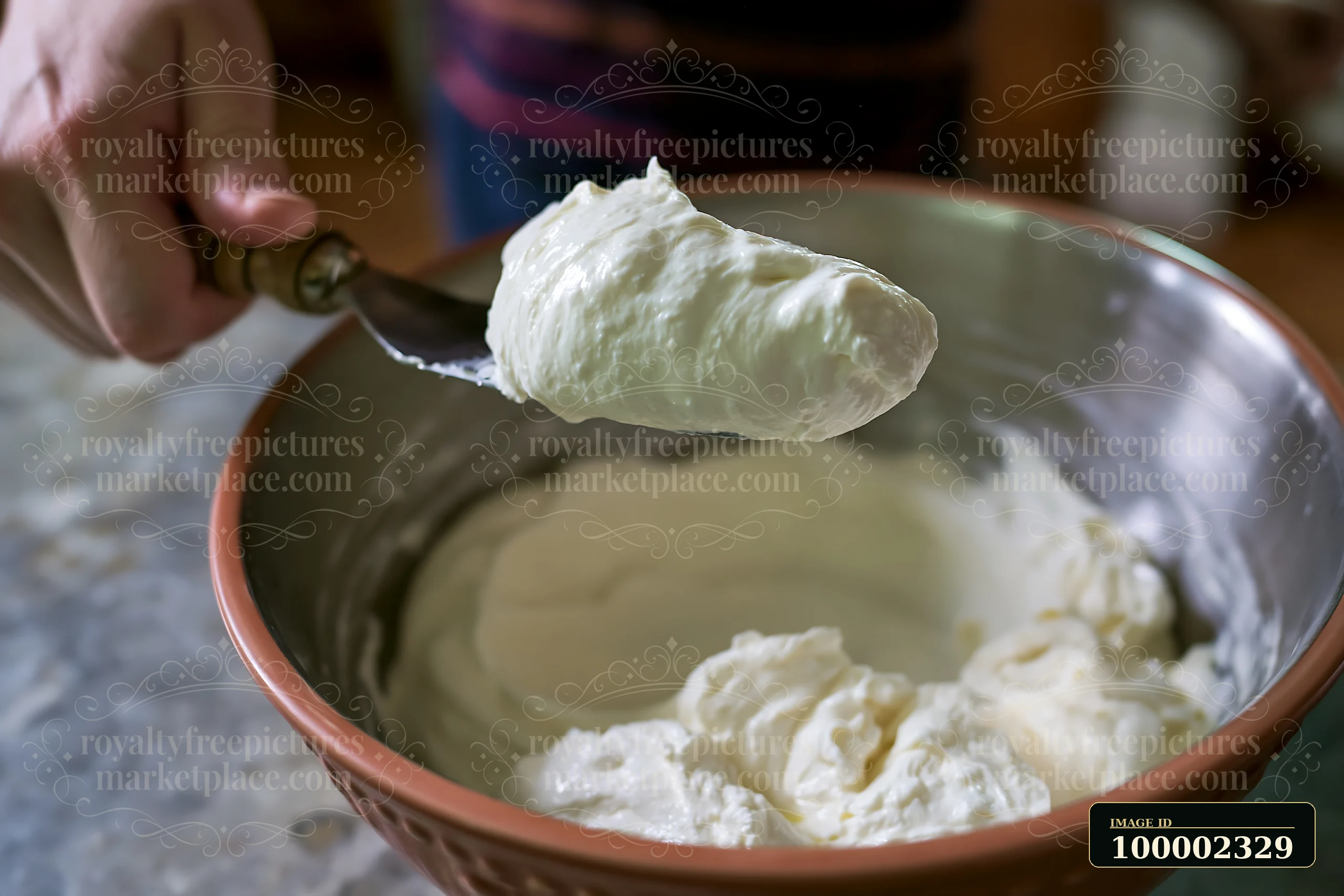 A person holds a spoonful of cream dose with smooth glossy texture above a bowl filled with a thick cream mixture.