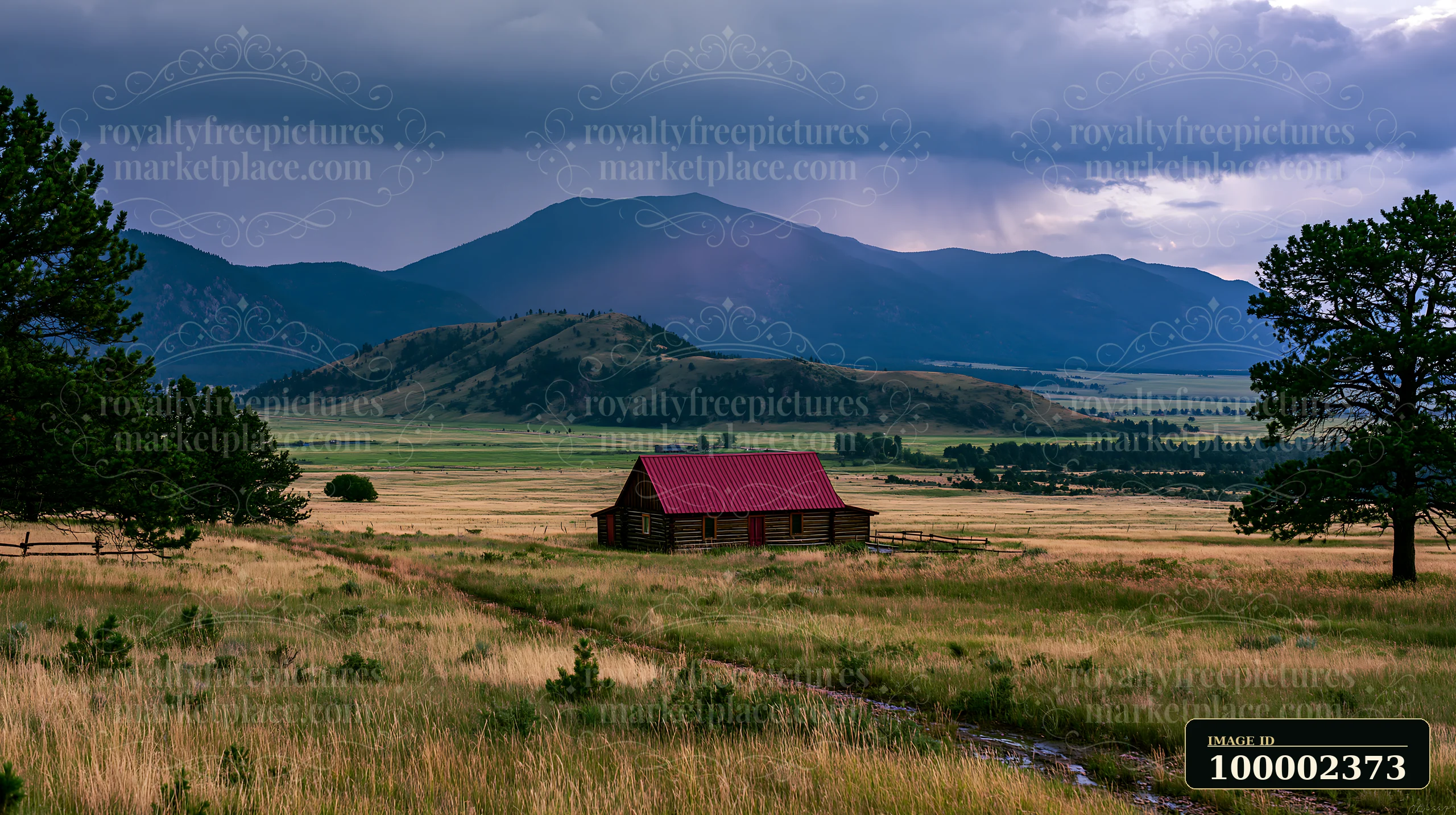 Dark clouds gather above a mountain range as a storm approaches a lonely cabin set in a grassy field.