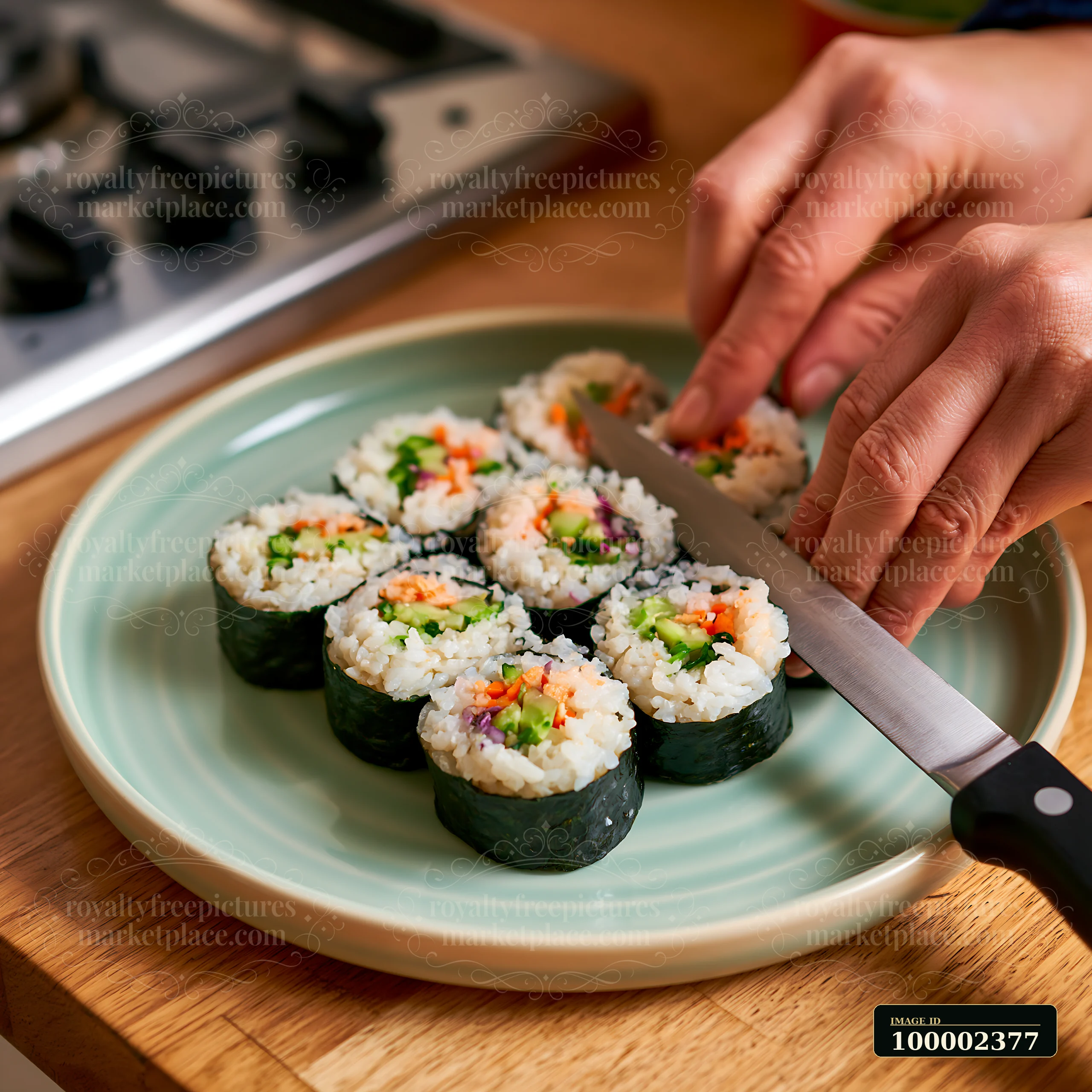 A person prepares sushi rolls being cut with knife on a plate in a modern kitchen.