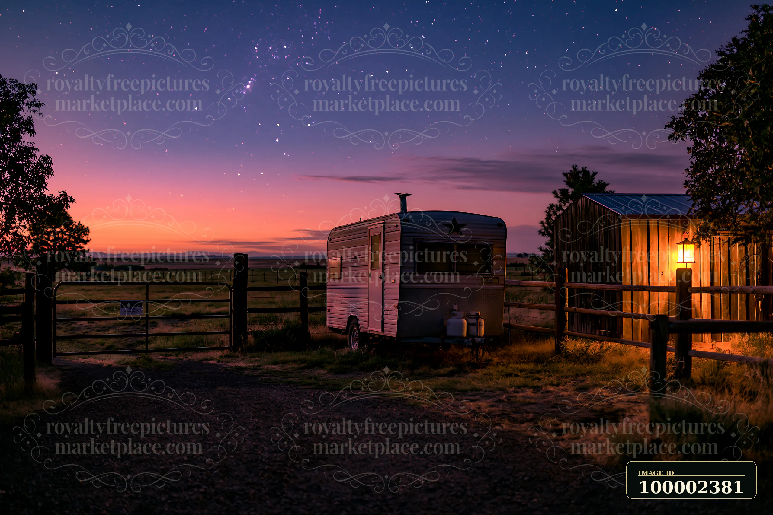 A horse trailer stands beside a wooden barn, illuminated by a light, under a starry sky at dusk.