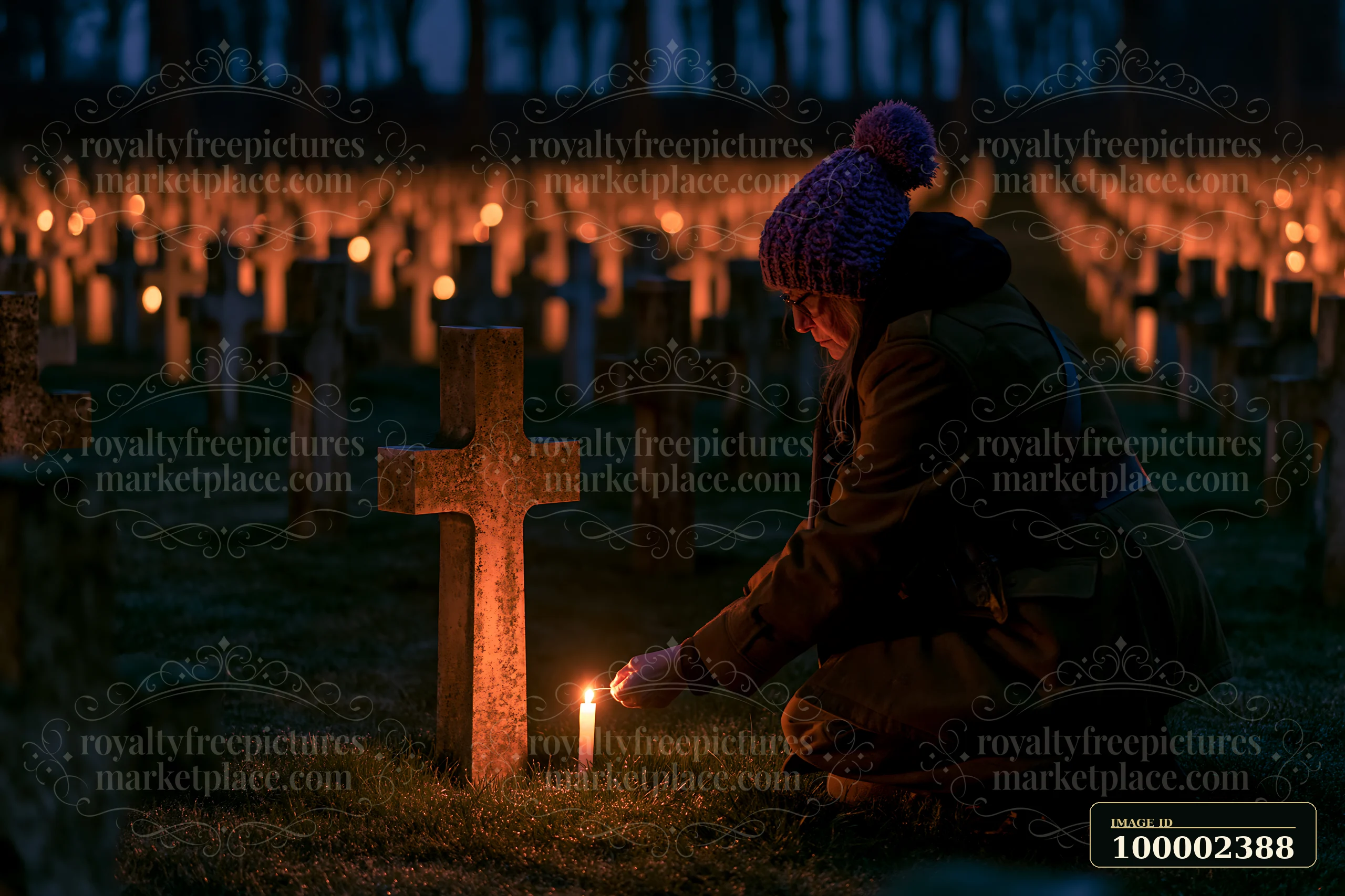 A person kneels at a war cemetery during nighttime, lighting a candle beside a grave cross.