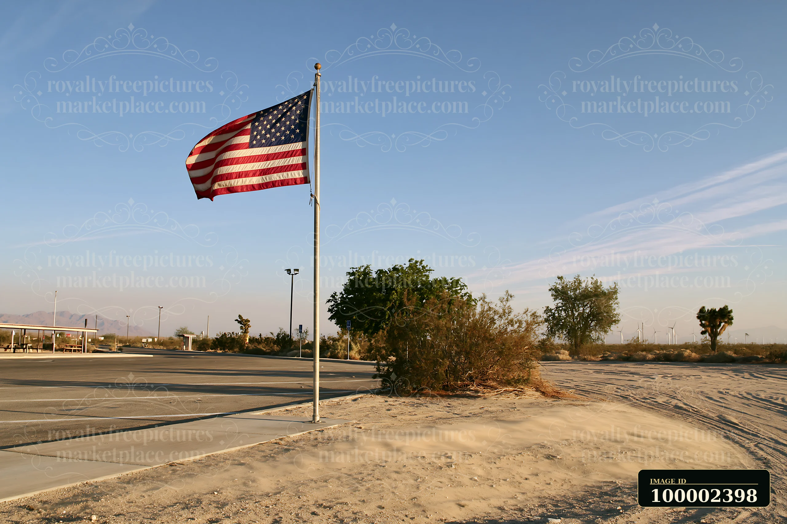 An American flag flying in strong wind stands tall at an empty parking lot surrounded by sparse vegetation.