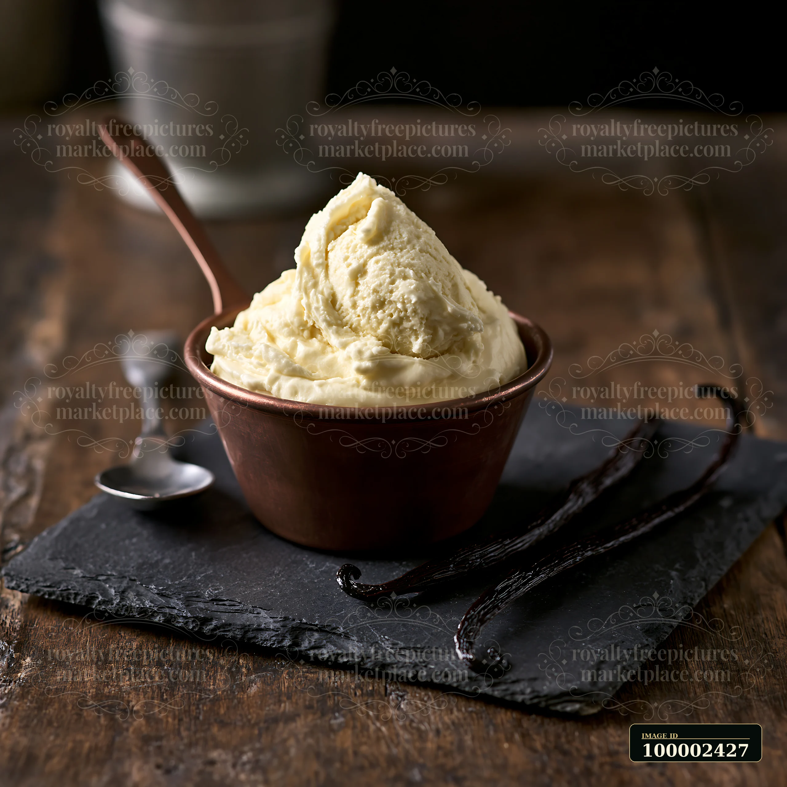 A bowl of cream sits on a dark stone surface, accompanied by vanilla pods.