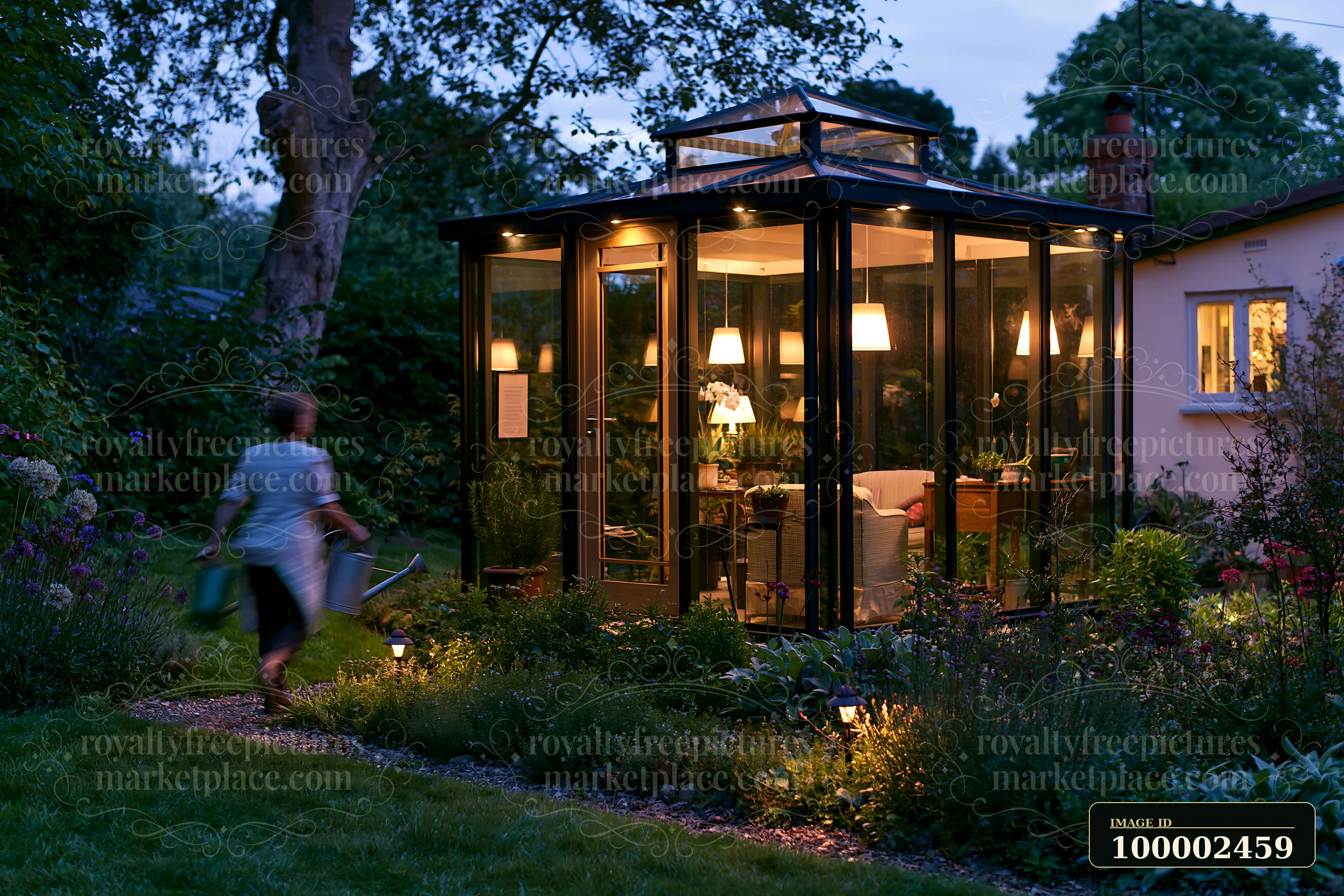A person walks in a garden carrying a watering can near a modern glass garden pavilion with night lighting.