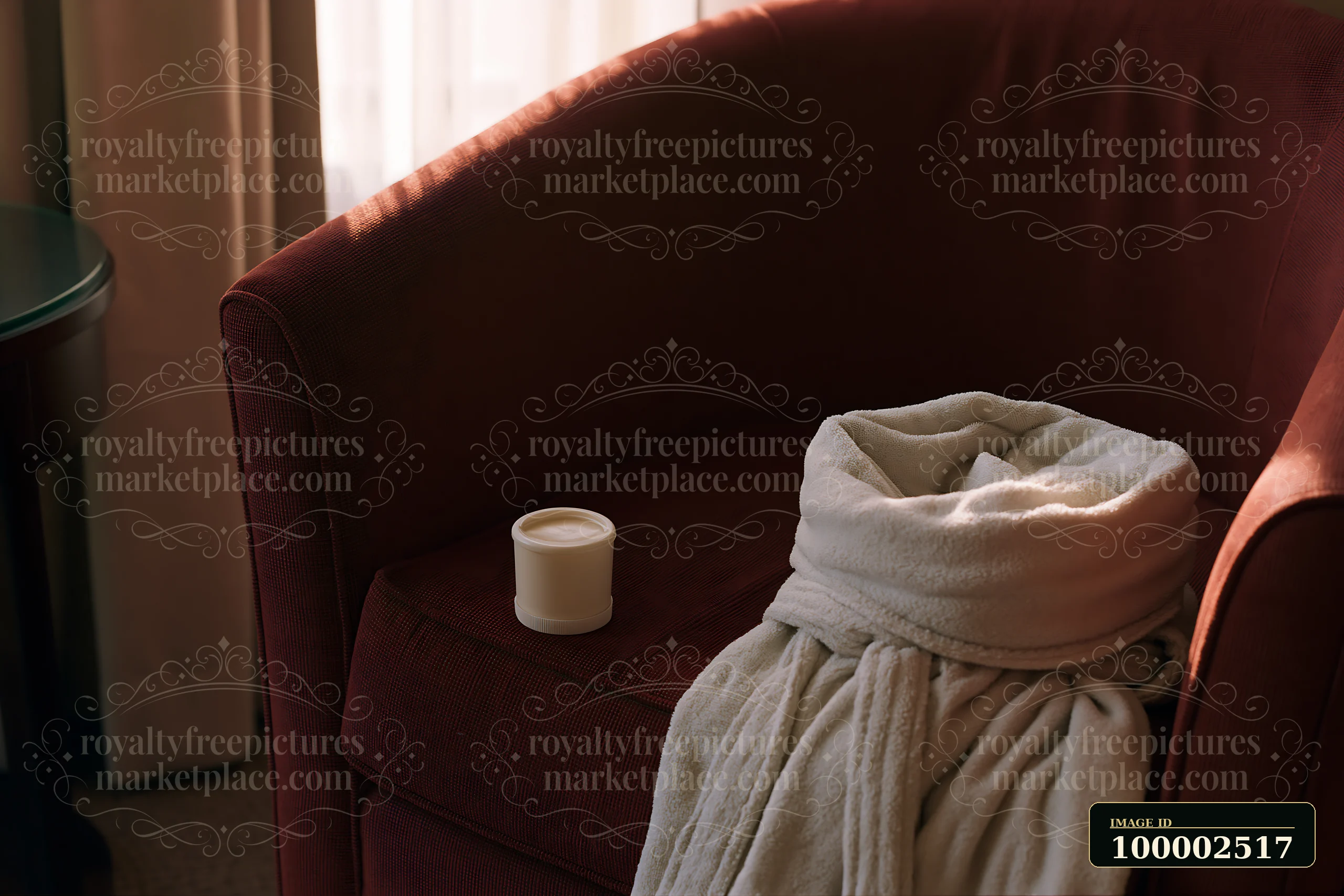 A cream dose sits beside a folded robe on a chair in a cozy space with soft light coming through a window.