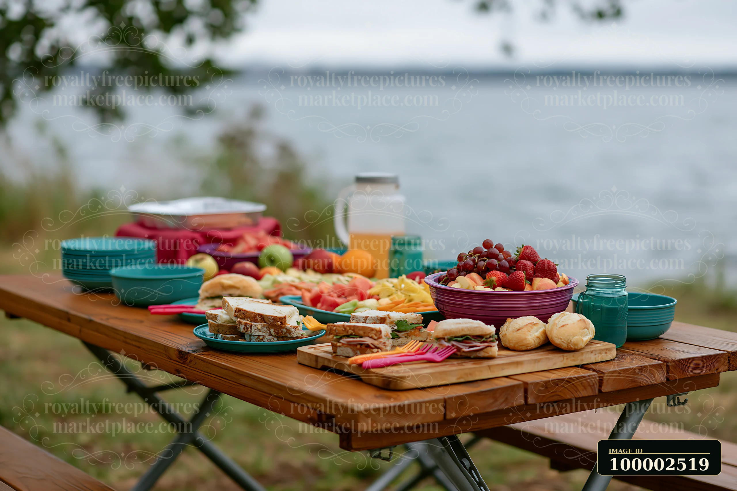 A zero waste buffet table filled with various fruits, sandwiches, and drinks is set along the water's edge.