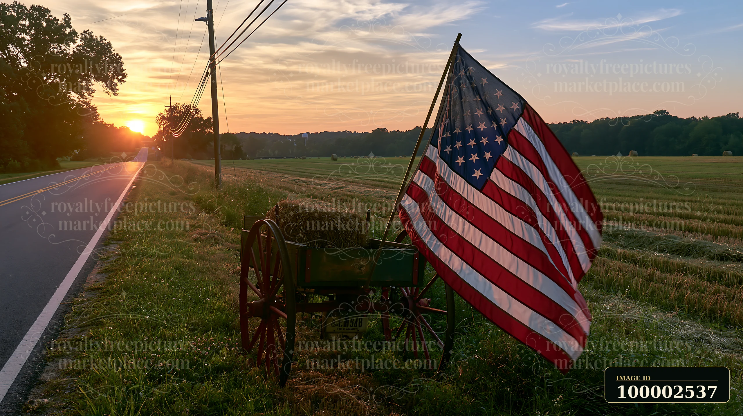 A vibrant American flag stands on a wooden cart beside a rural road as the sun sets over the fields.