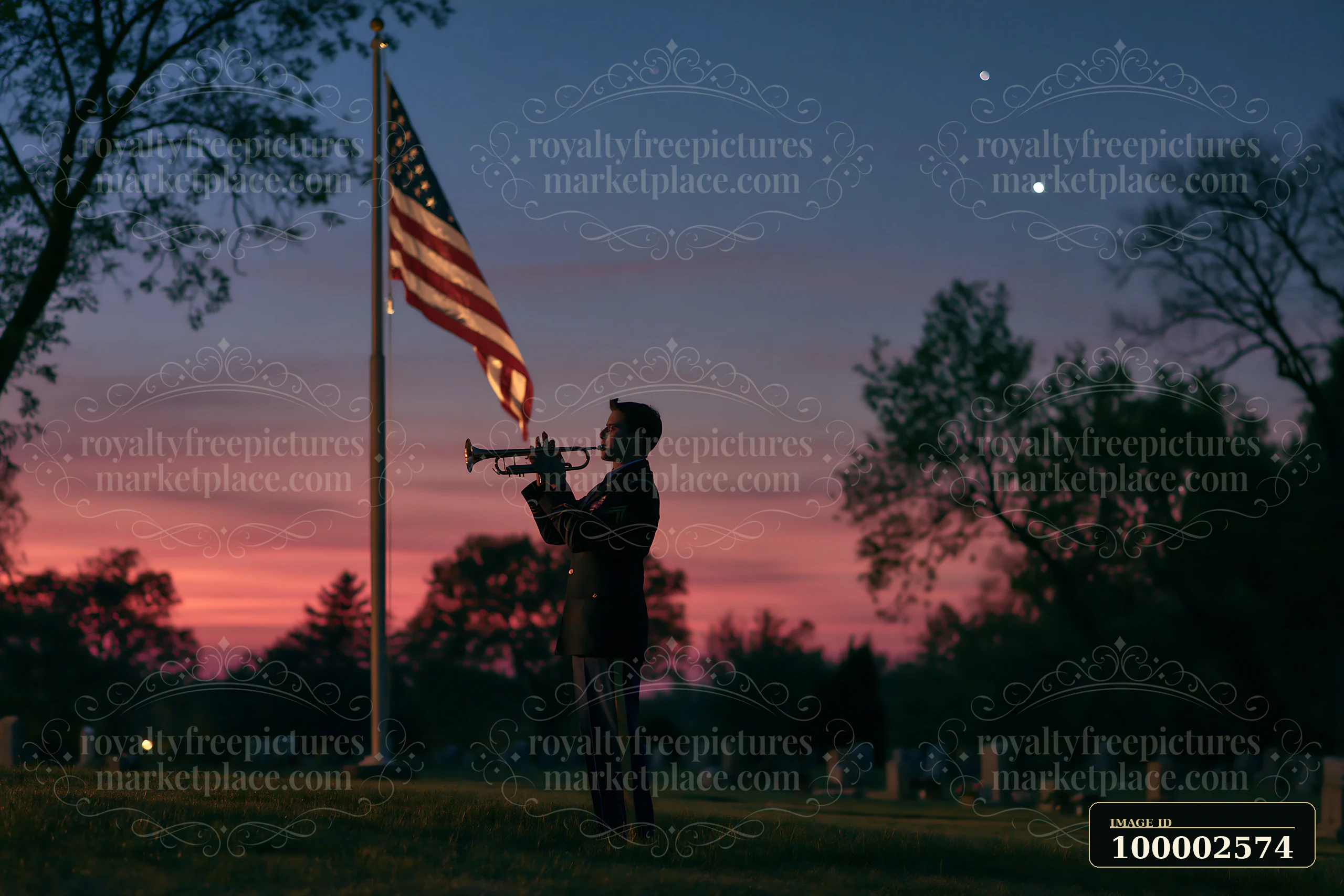 A person plays a trumpet near a flagpole with an American flag in a cemetery at dusk.