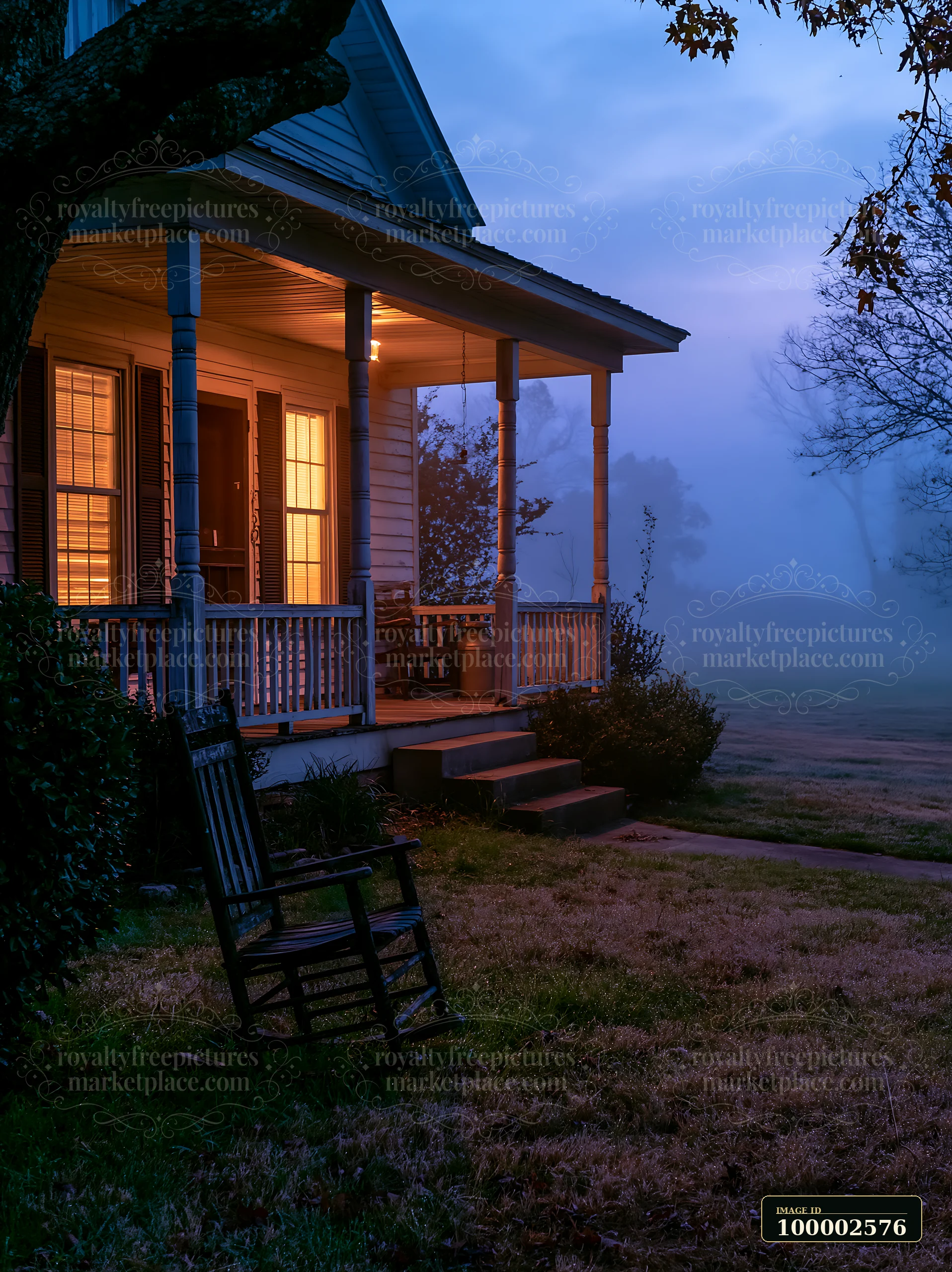 A rural farmhouse stands with its porch illuminated in the morning fog.