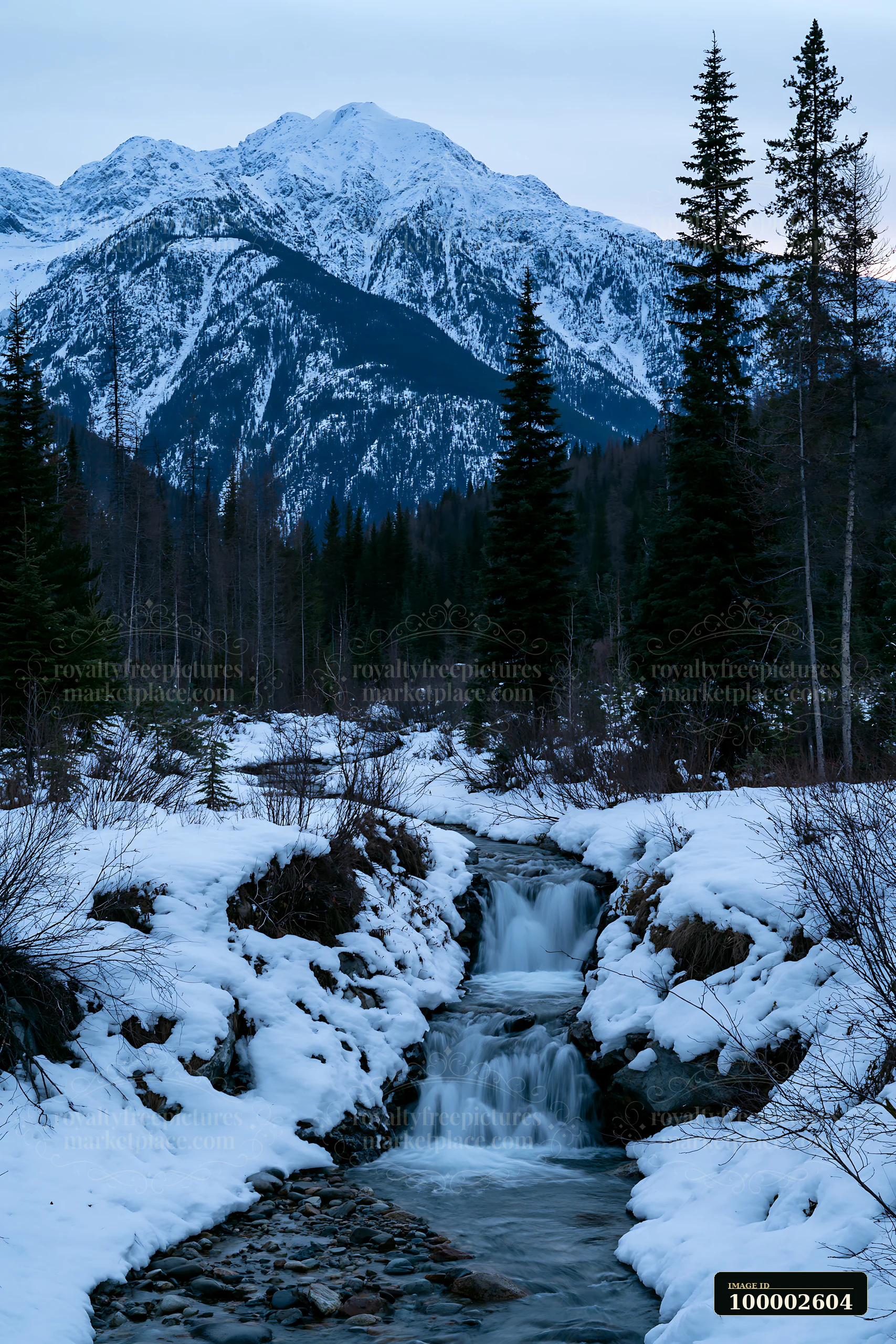 A waterfall flows through a snowy landscape with tall trees and majestic snowy peaks in the background.