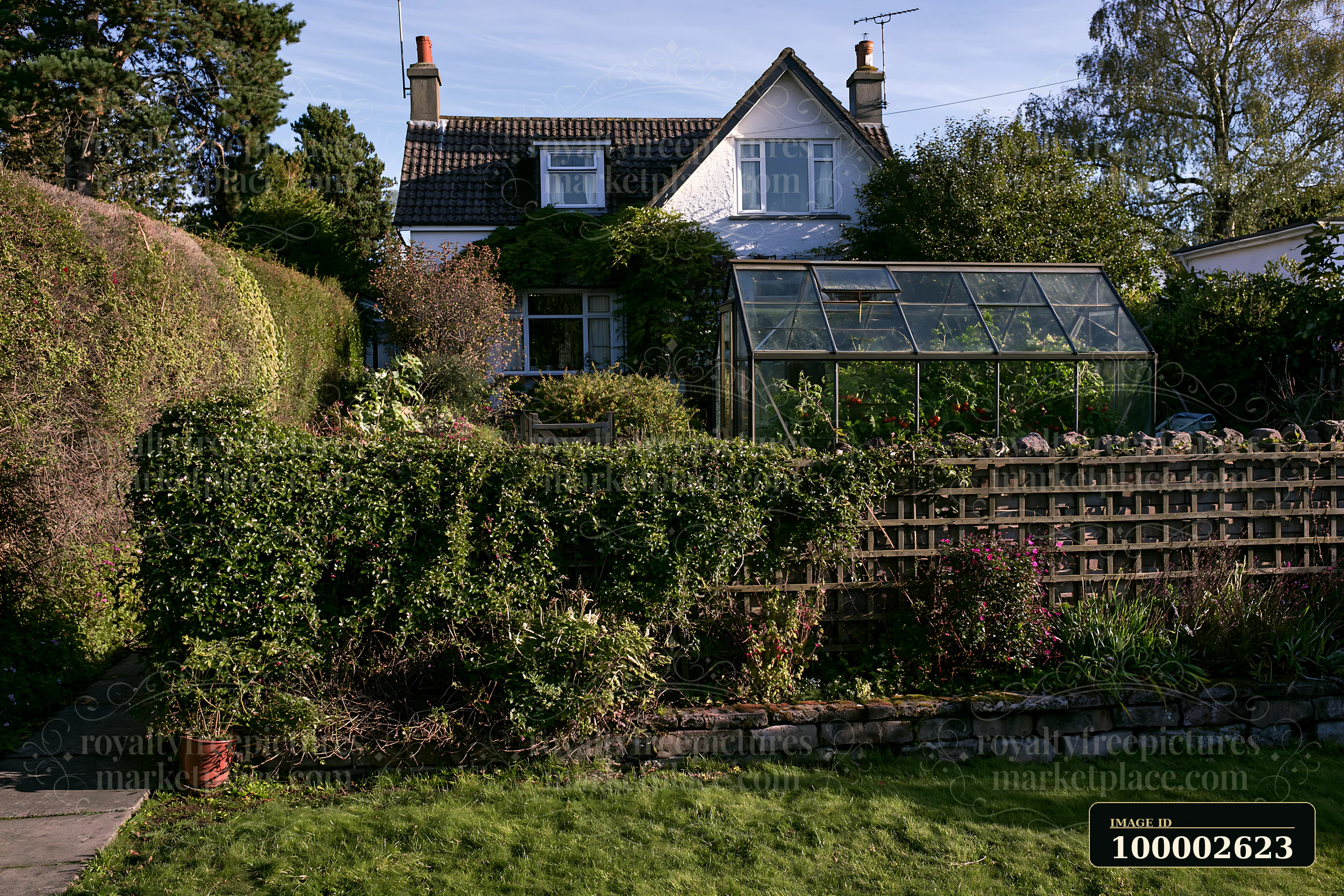 A country house surrounded by hedges features a greenhouse and a garden filled with plants.