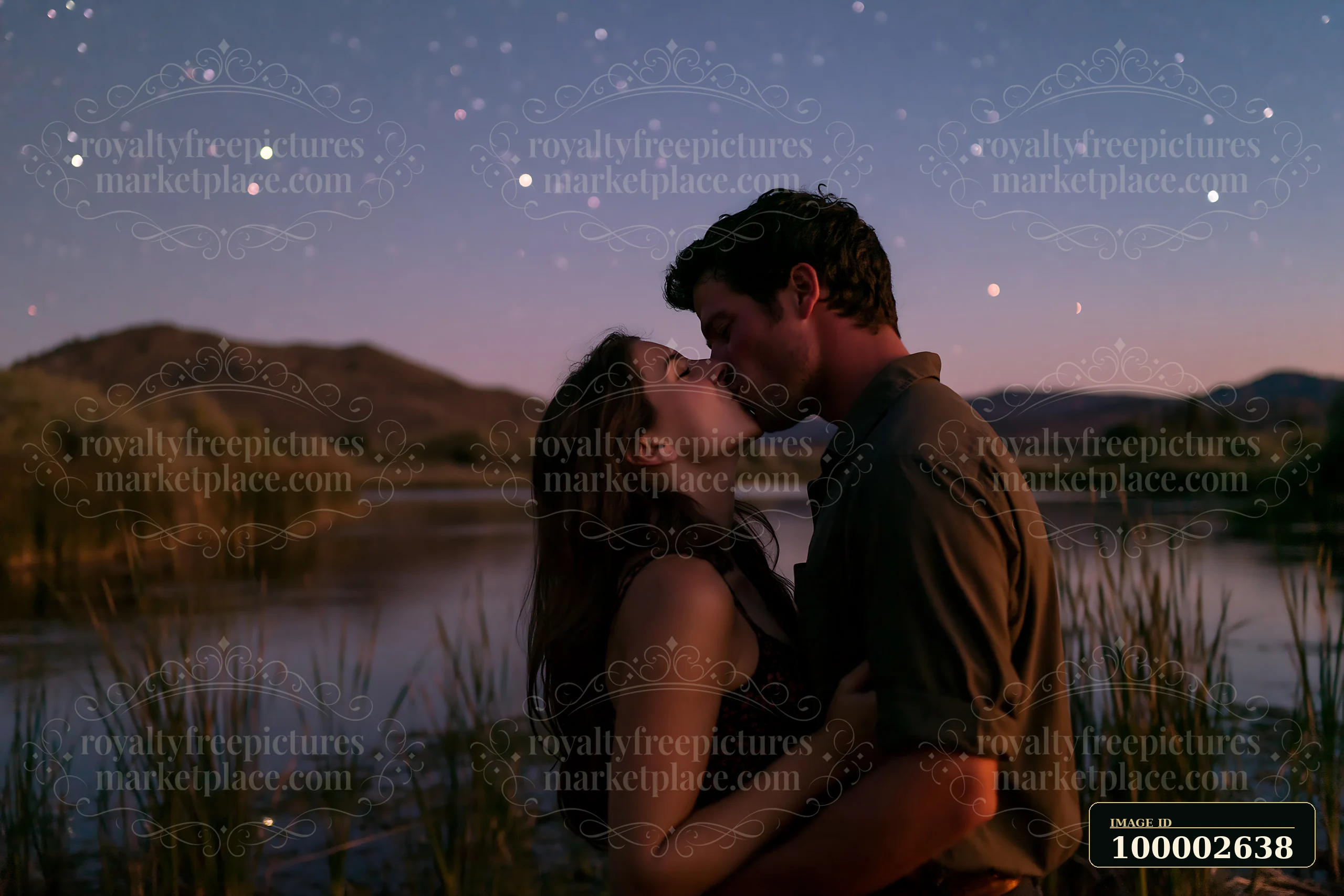 A happy couple kissing beneath stars in nature by a calm water body surrounded by grass and hills at dusk.
