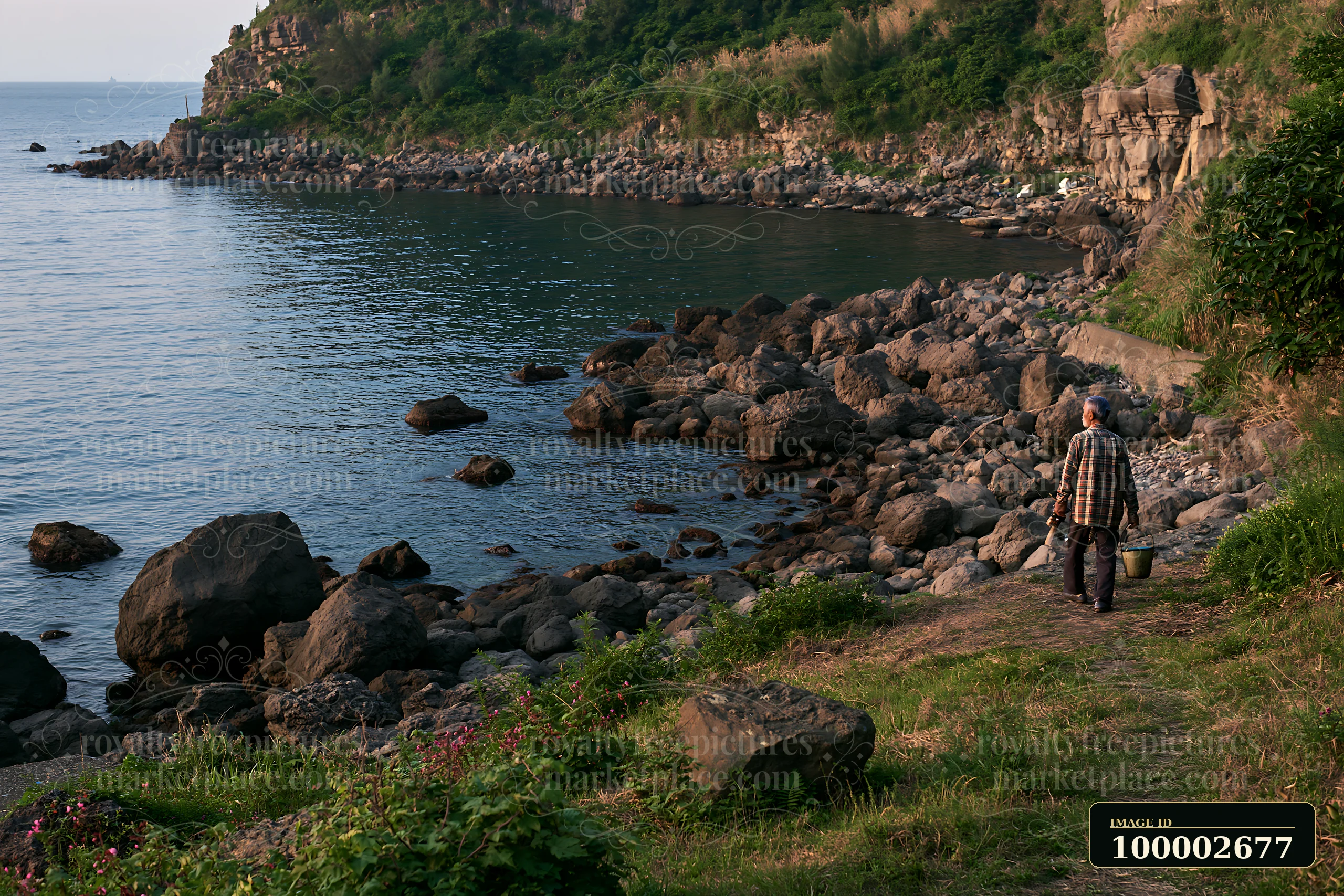 A person walks along a rocky coastline with exposed rocks in the foreground and water in the background.