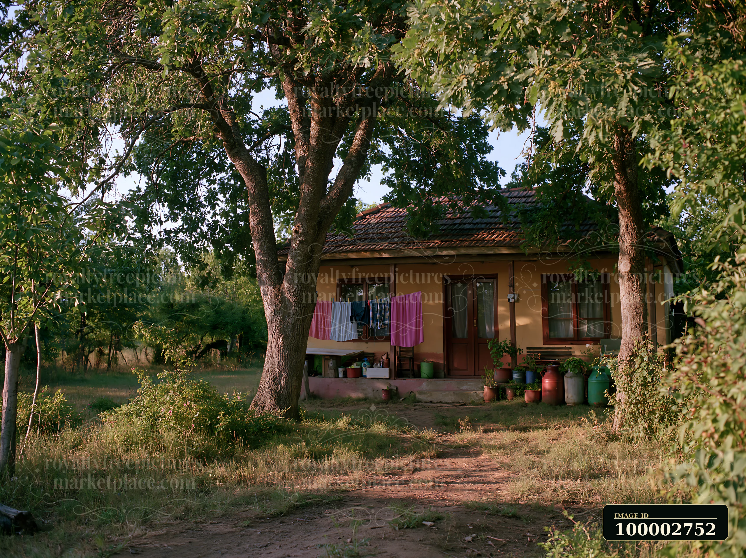 A rural home under oak trees features a porch with laundry hanging to dry.