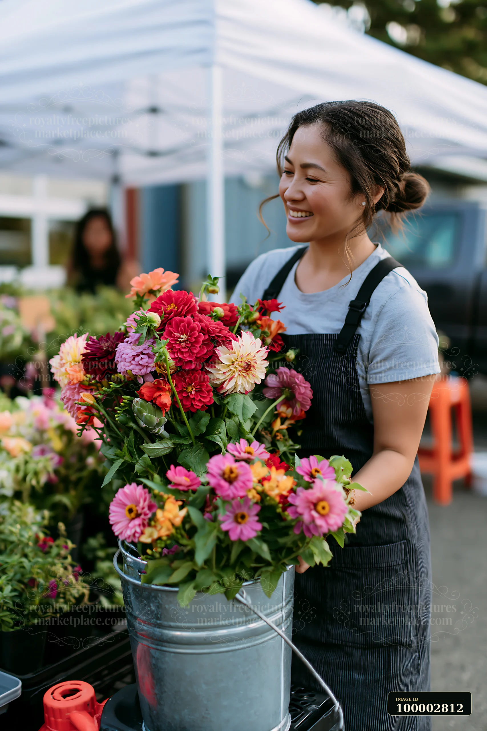 A woman arranges mixed seasonal flowers at a farmers market.