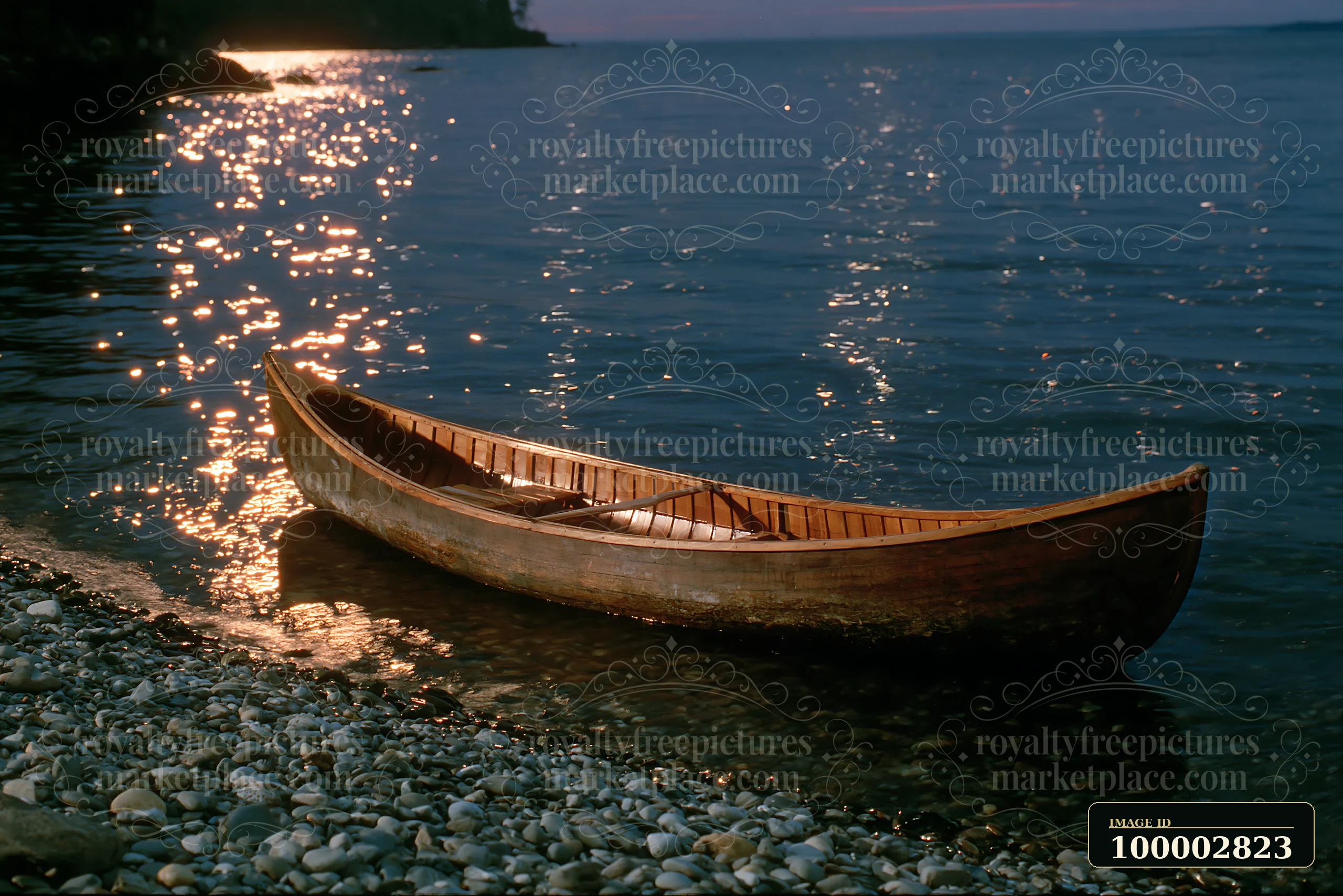 A canoe rests on pebbles by the water as stars shine brightly in the night sky.