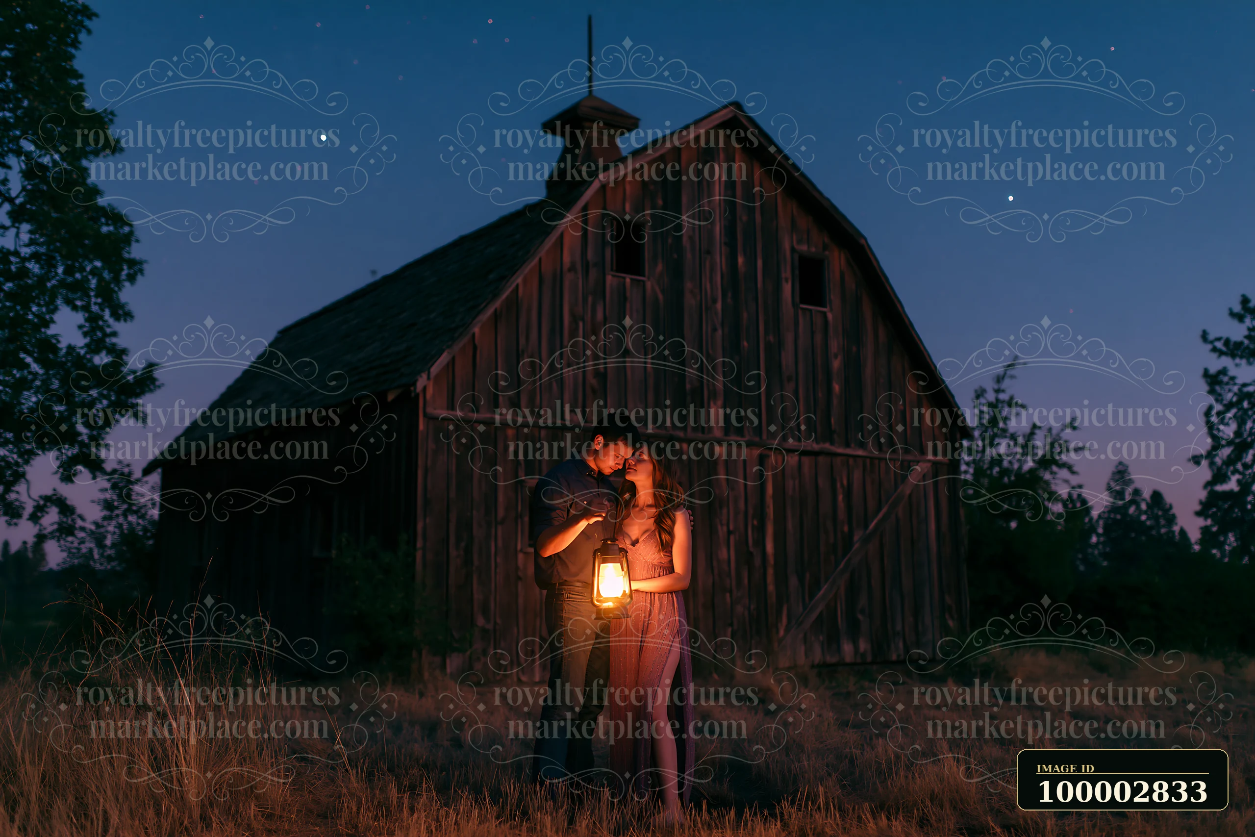 A couple holding a lantern beneath stars stands close together near a rustic barn.